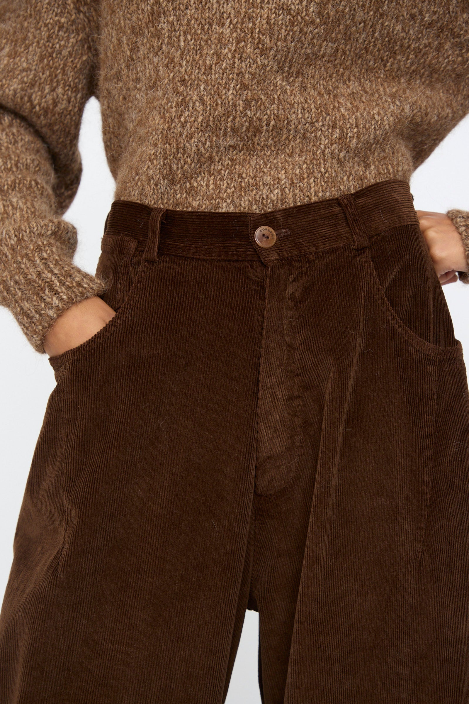 Someone wearing Cordera's Corduroy Baggy Pants in Brown with an elastic waistband, paired with a chunky brown knit sweater, hands in their pockets.