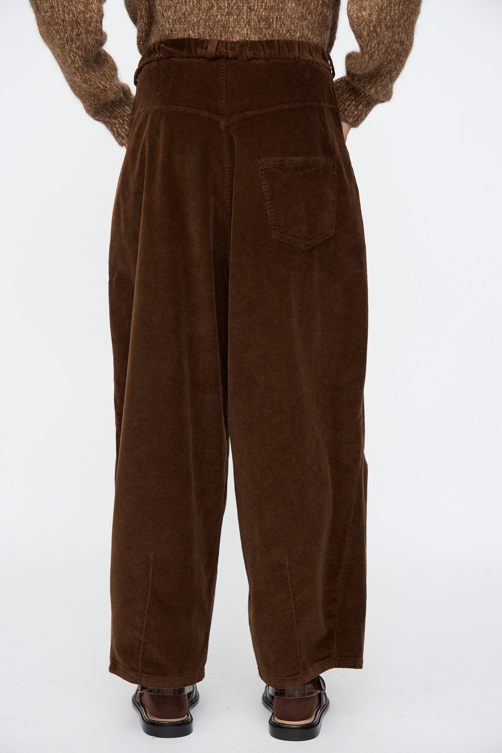 Person wearing Cordera's Corduroy Baggy Pants in Brown, viewed from the back with hands behind their back, styled with a brown textured sweater.