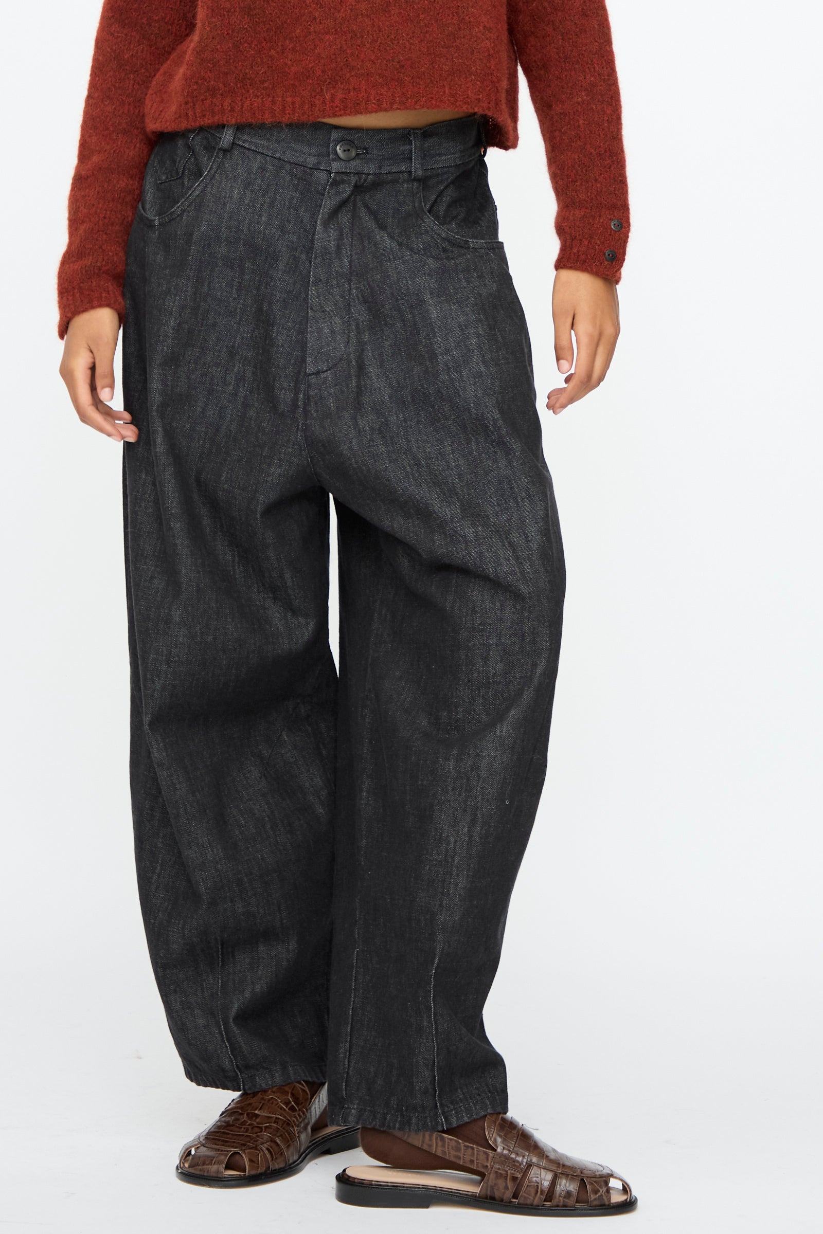 Person wearing Cordera Denim Baggy Pants in Black, paired with a rust sweater and brown open-toe sandals, photographed from shoulders down against a plain background.