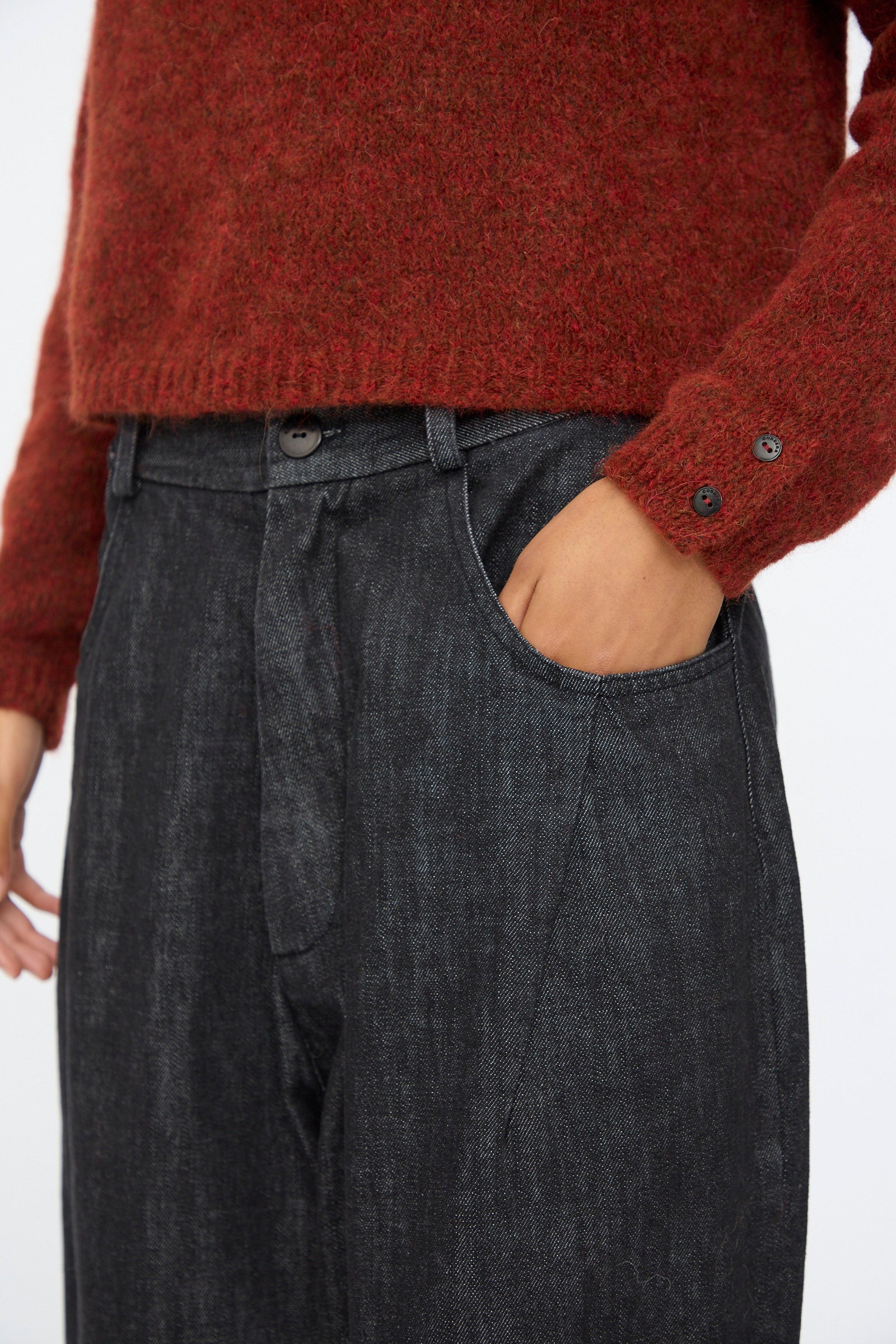 A person wears Cordera's Denim Baggy Pants in Black, styled high-waisted for a relaxed, loose fit, paired with a red textured long-sleeve sweater and one hand casually placed in the pocket.