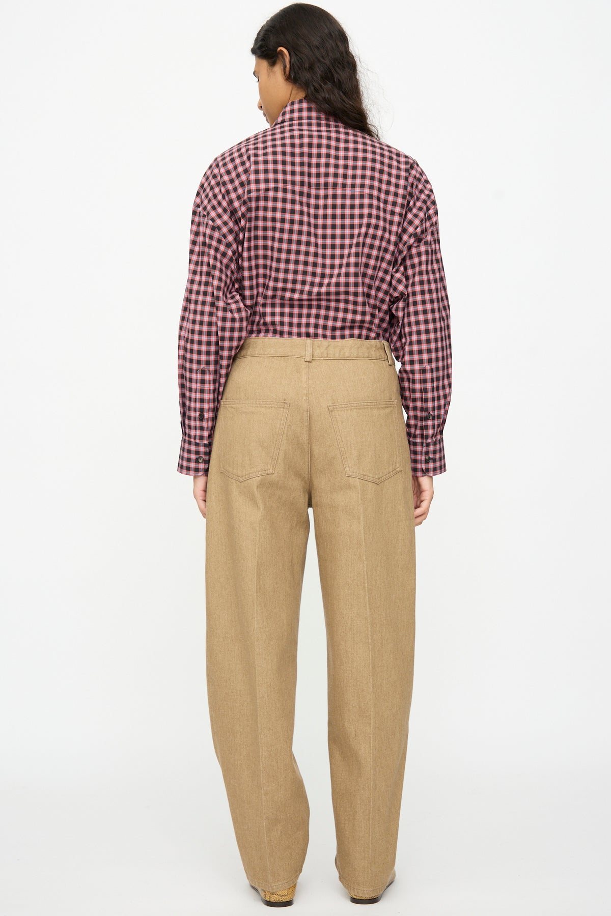 A person seen from behind wears a red and black plaid button-down shirt tucked into beige Cordera Denim Carrot Pants with back pockets and a tapered leg.