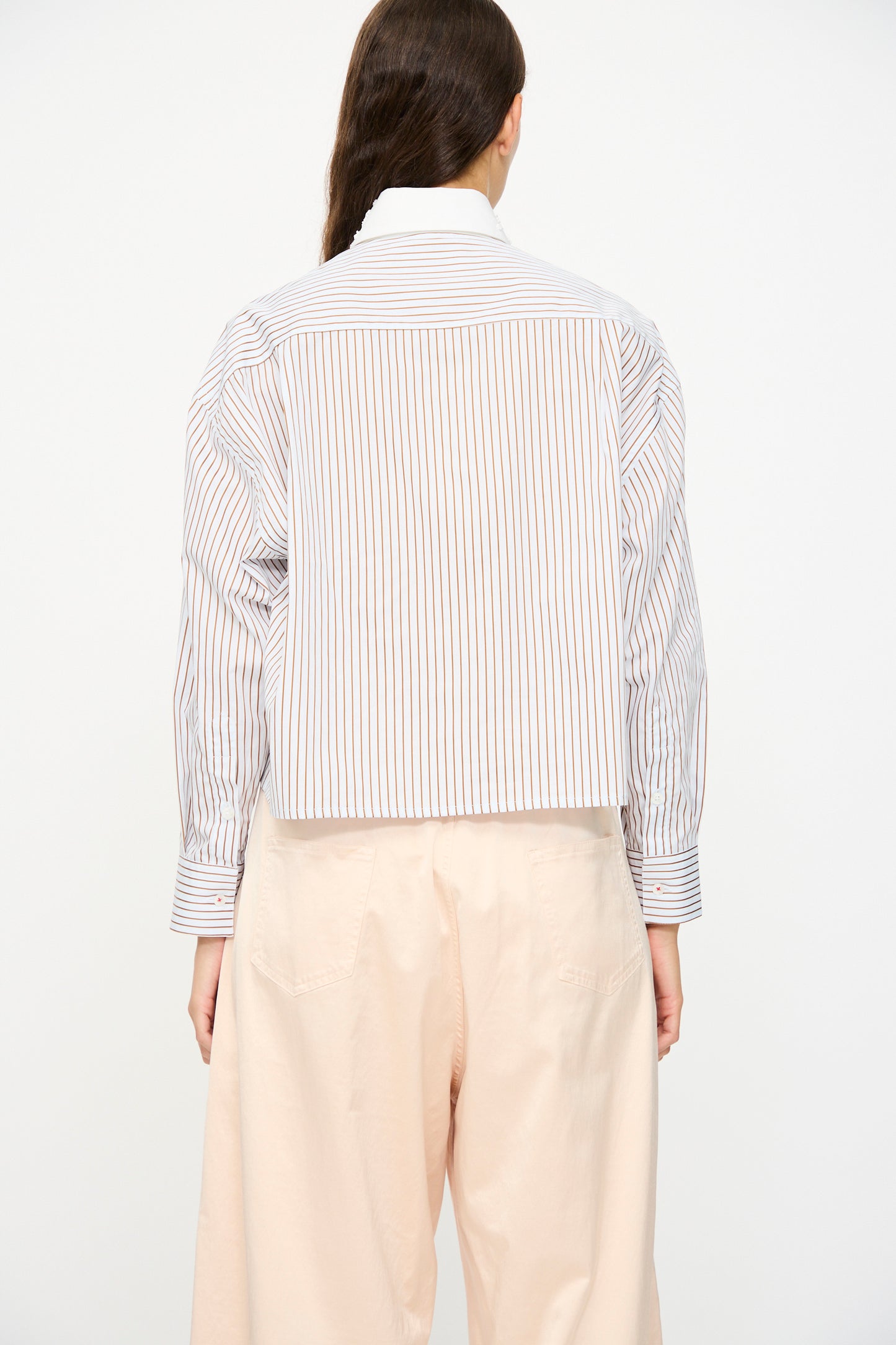 A person seen from the back wears Cordera's Embellished Shirt in blue and white stripes, made in Spain, paired with loose light beige pants.
