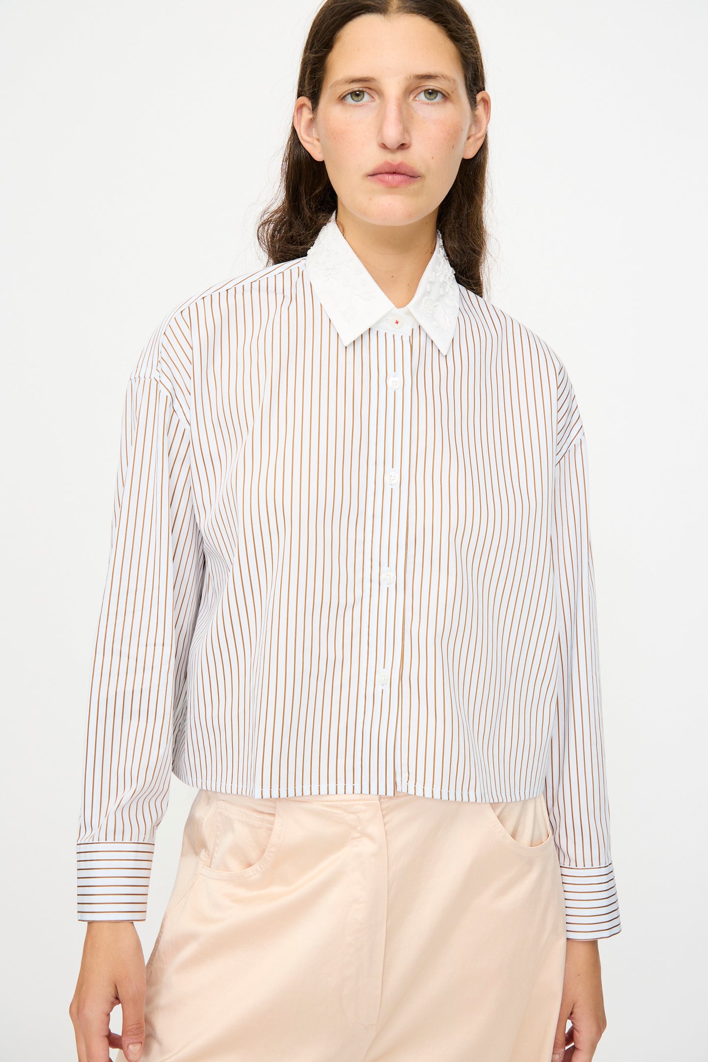 A woman wears the Cordera Embellished Shirt in Striped with a white collar, paired with light beige pants, standing against a plain white background.