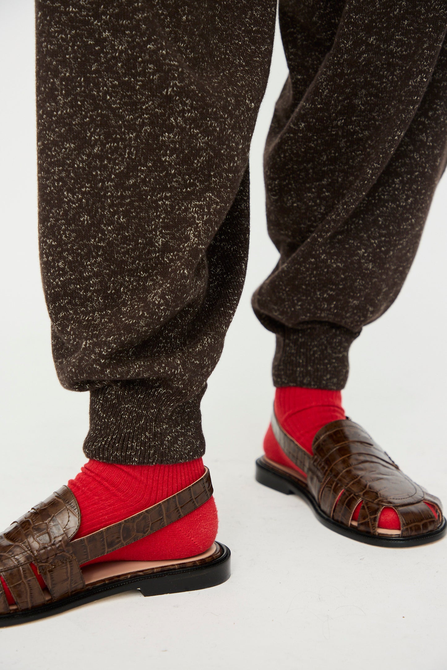 A person wears Cordera's Flecked Cotton Pant in Brown, paired with bright red socks and brown sandals. Only the lower legs and feet are visible against a plain background.