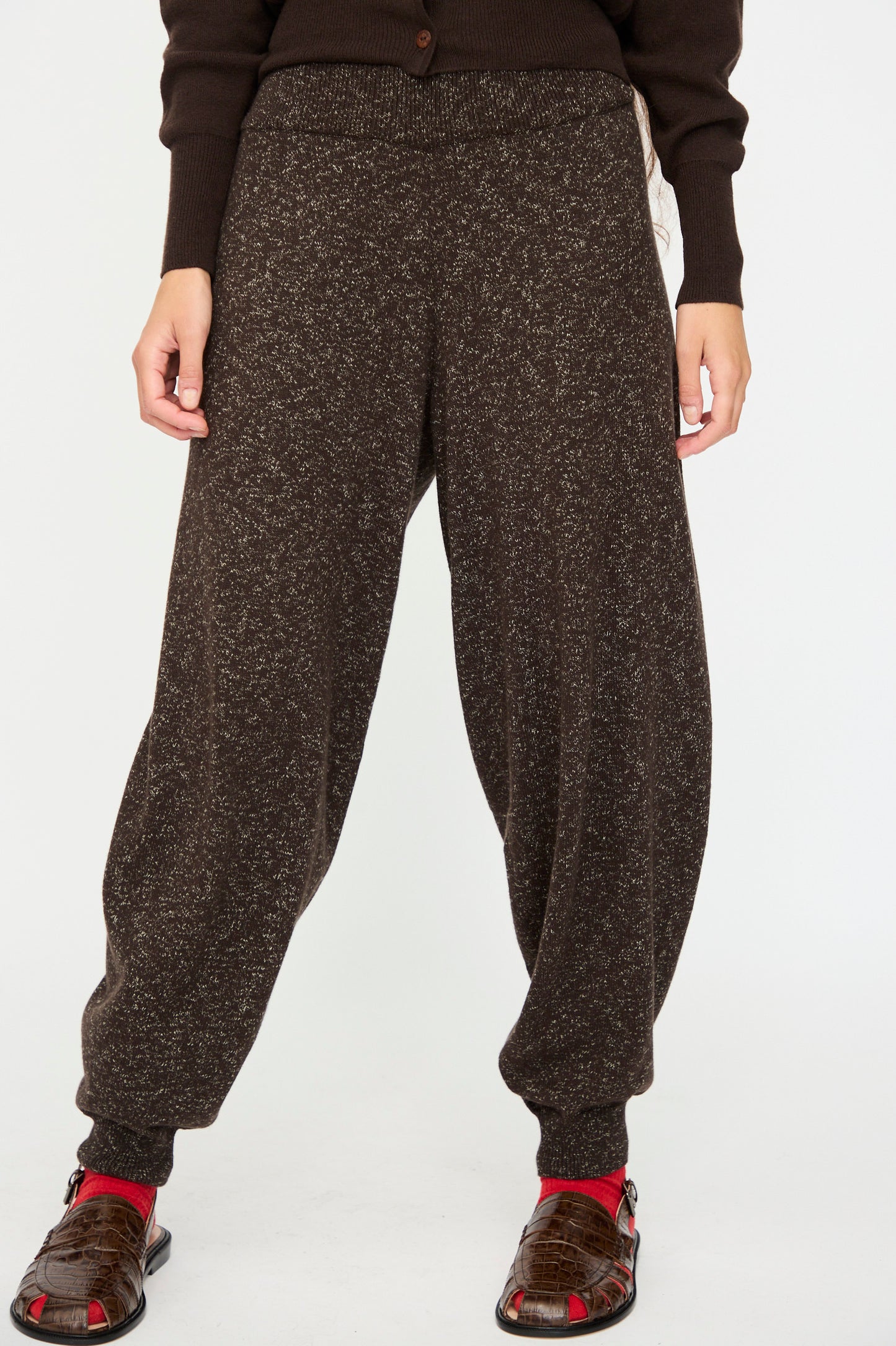 Person wearing Cordera's Flecked Cotton Pant in Brown, paired with a dark brown sweater, red socks, and brown sandals—standing against a plain white background.