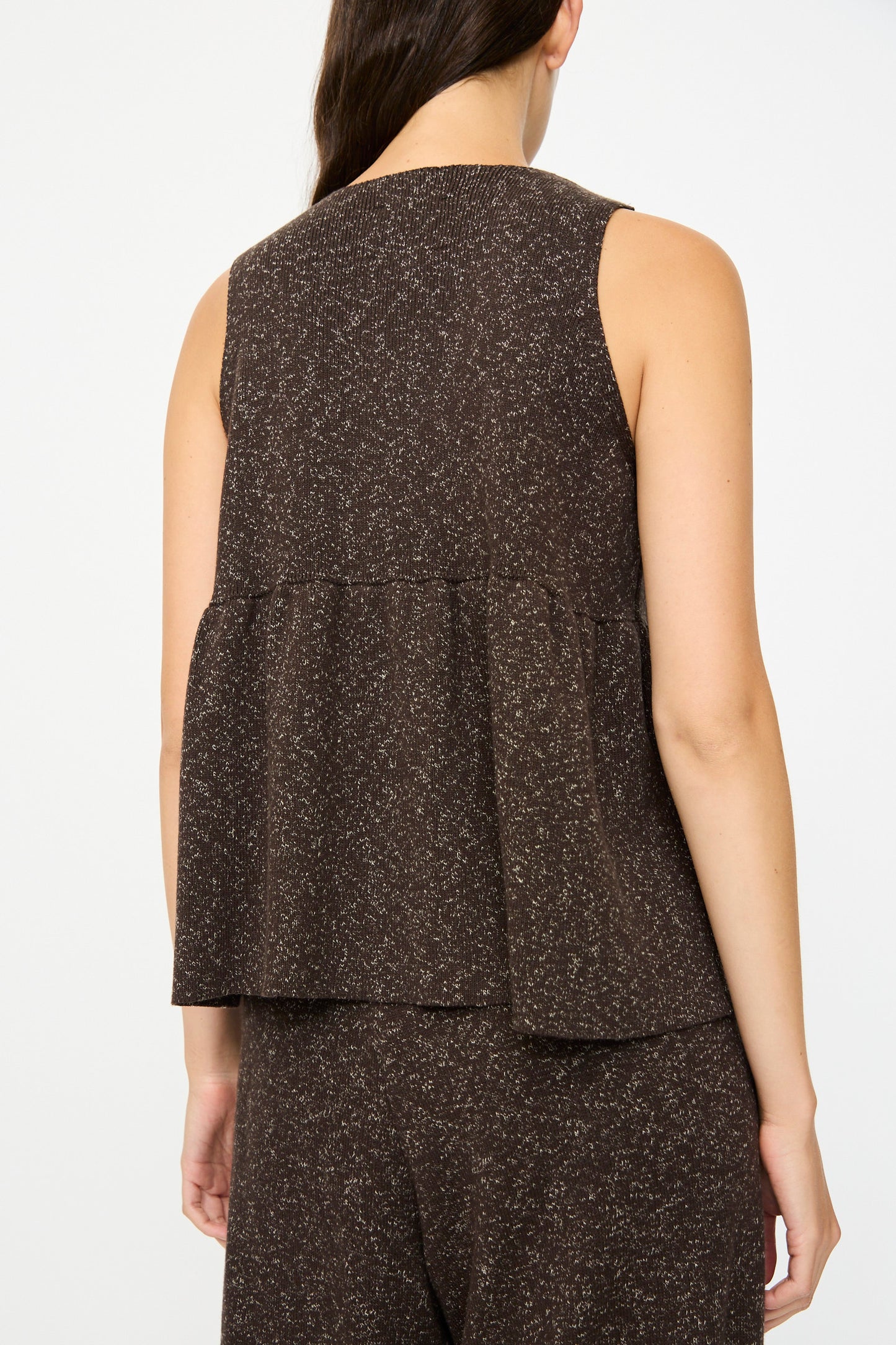 A woman is seen from the back wearing Cordera’s Flecked Cotton Peplum Top in brown, a sleeveless design with a loose, flared peplum silhouette, paired with matching pants.