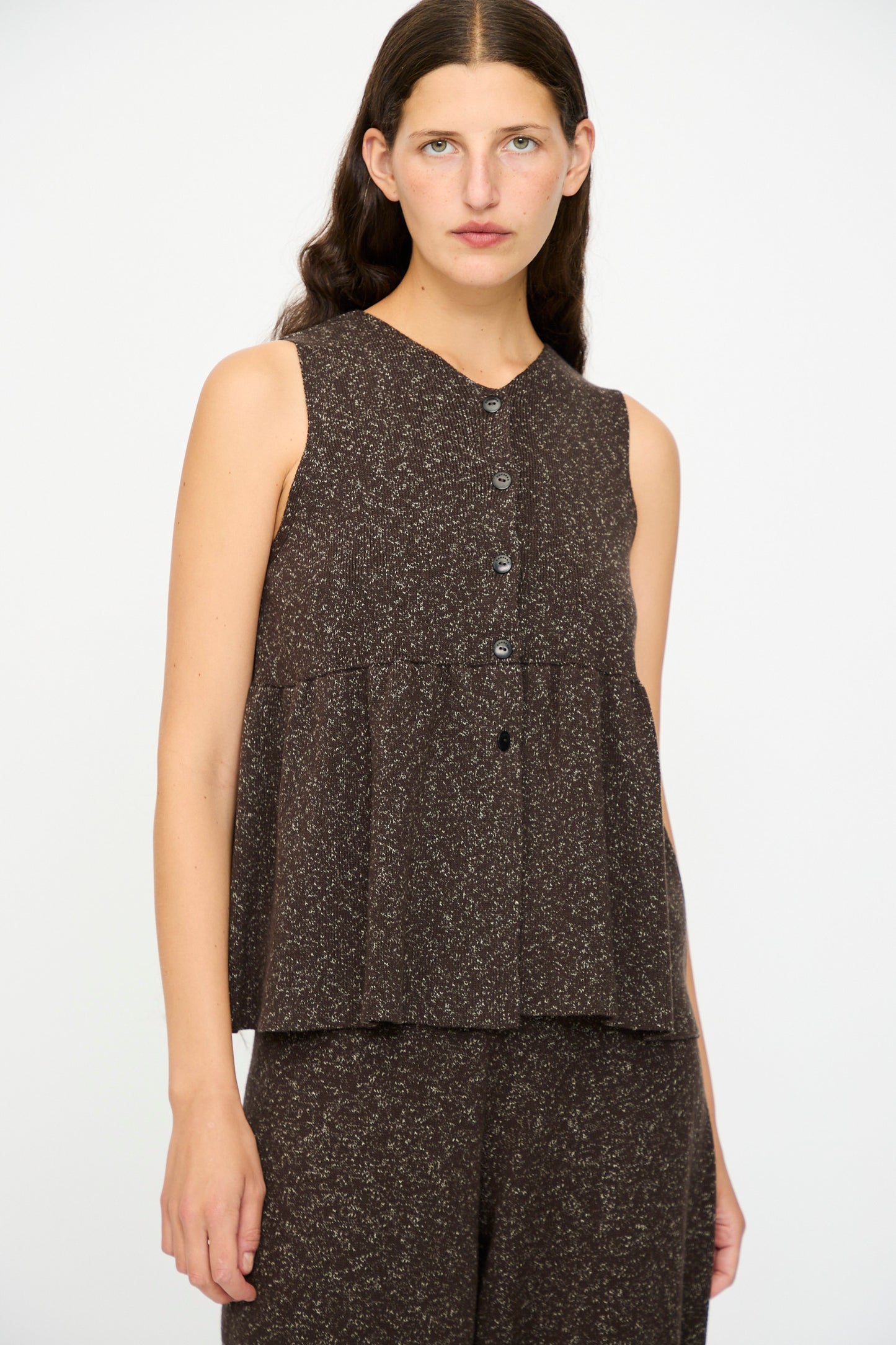 A woman with long brown hair wears the Cordera Flecked Cotton Peplum Top in Brown, styled with matching pants. She stands against a plain white background.