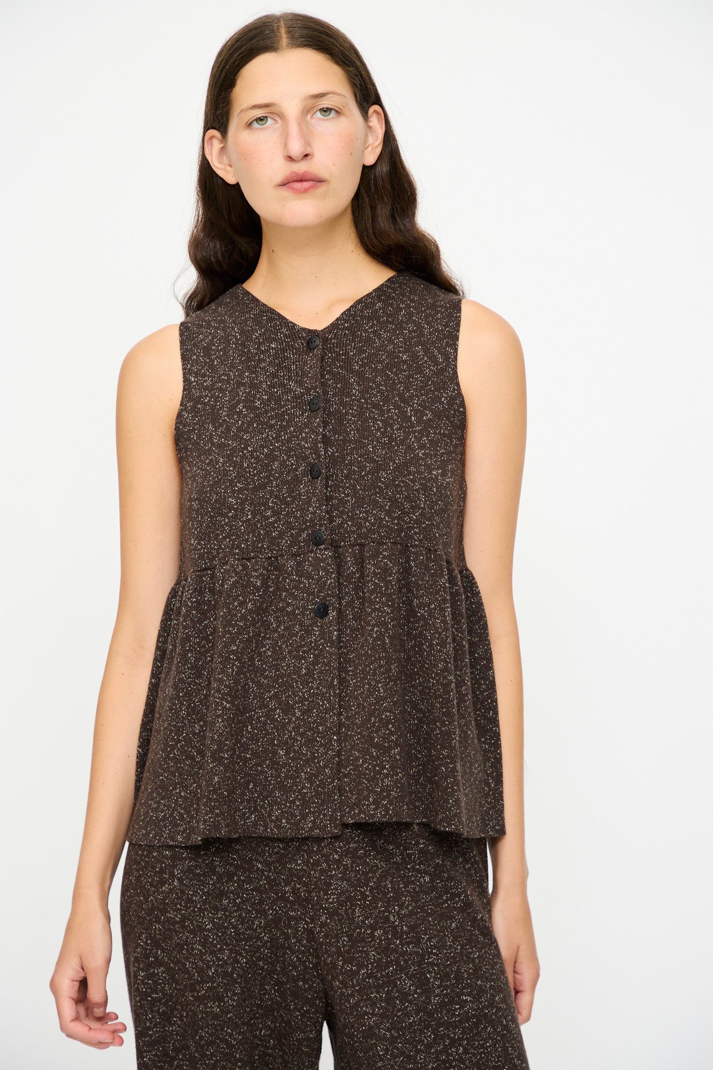 A woman with long brown hair wears the Cordera Flecked Cotton Peplum Top in Brown, paired with matching pants, standing against a plain white background.