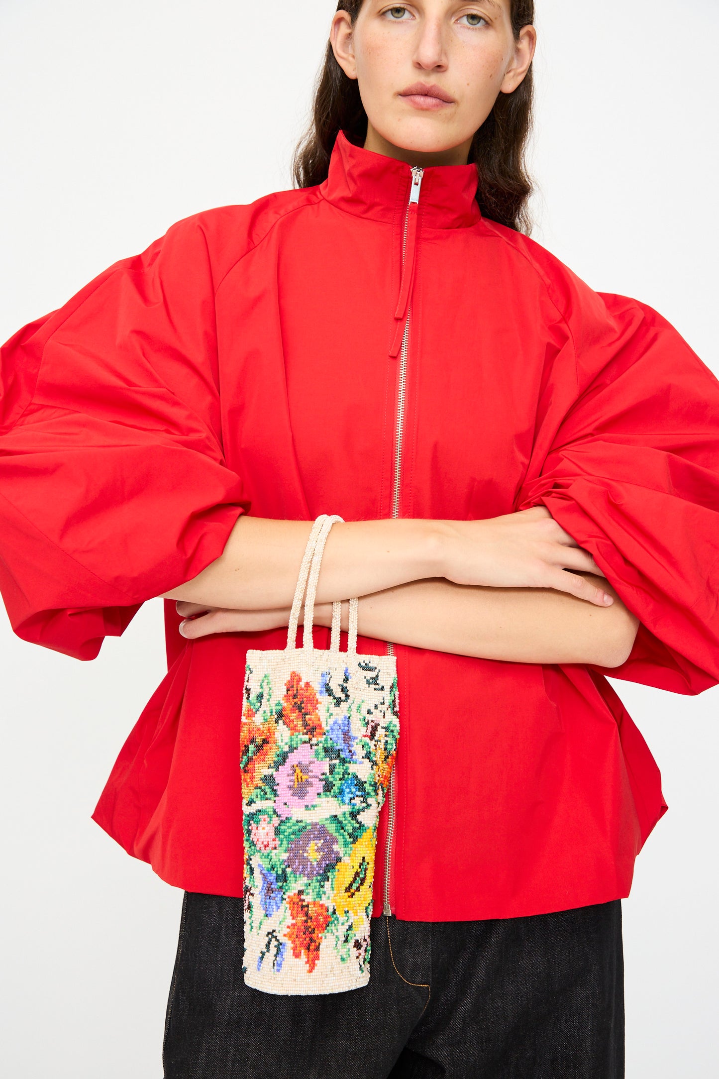 A person in a red zip-up jacket holds Cordera’s Handmade Beaded in Crisantemo bag, featuring a vibrant floral pattern with beautiful beading, handcrafted in Guatemala.