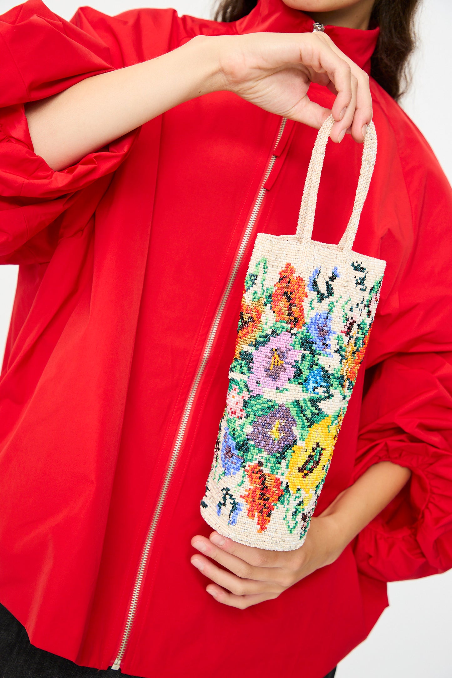 A person in a red jacket holds the Handmade Beaded in Crisantemo by Cordera, a vibrant, handcrafted bag featuring a colorful floral design.