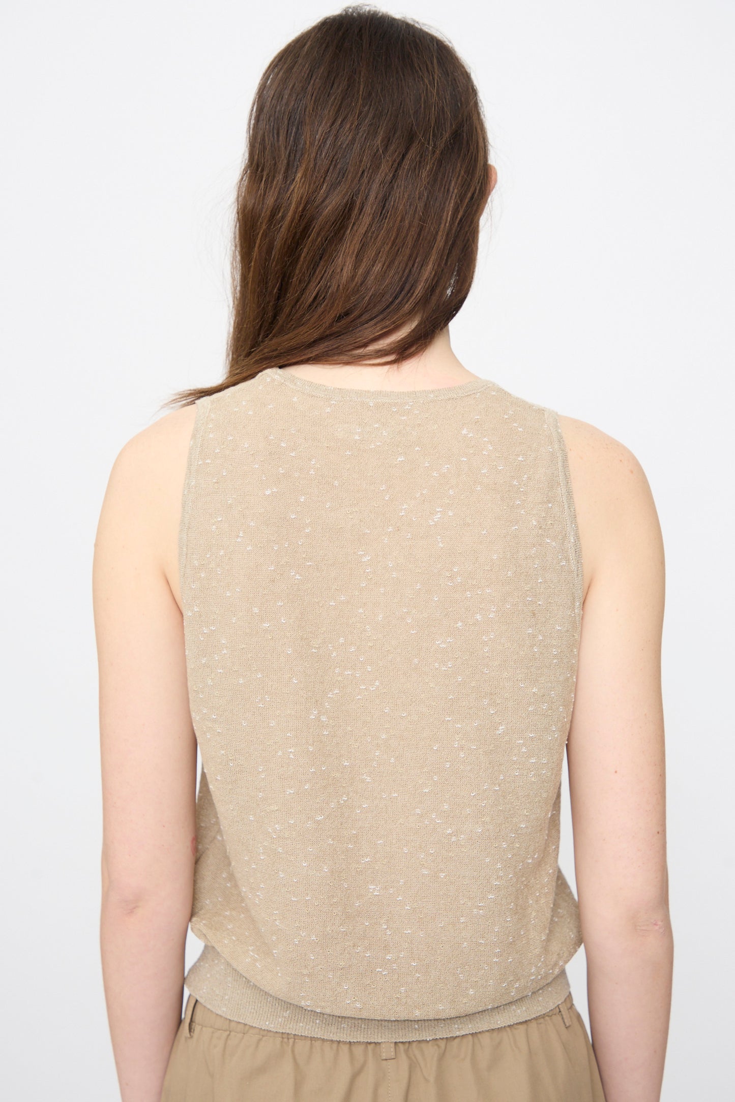 A person with long brown hair is shown from the back, wearing Cordera’s Linen and Cotton Flecked Tank Top in Beige against a plain background, paired with light brown pants.