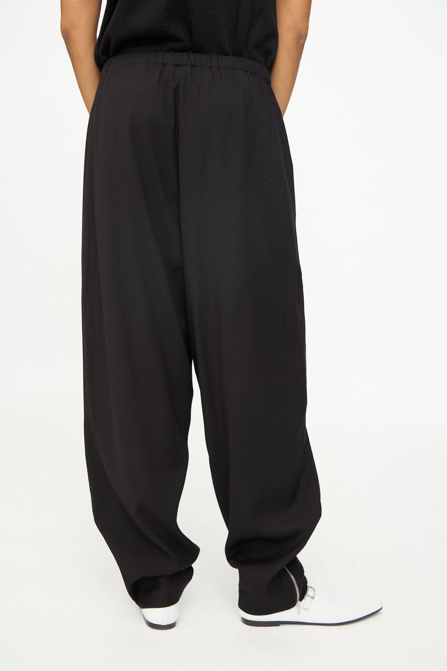 A person is shown wearing the Cordera Lounge Pants in Black, featuring a loose fit and elastic waistband, paired with white shoes and standing with hands behind their back against a plain white background.