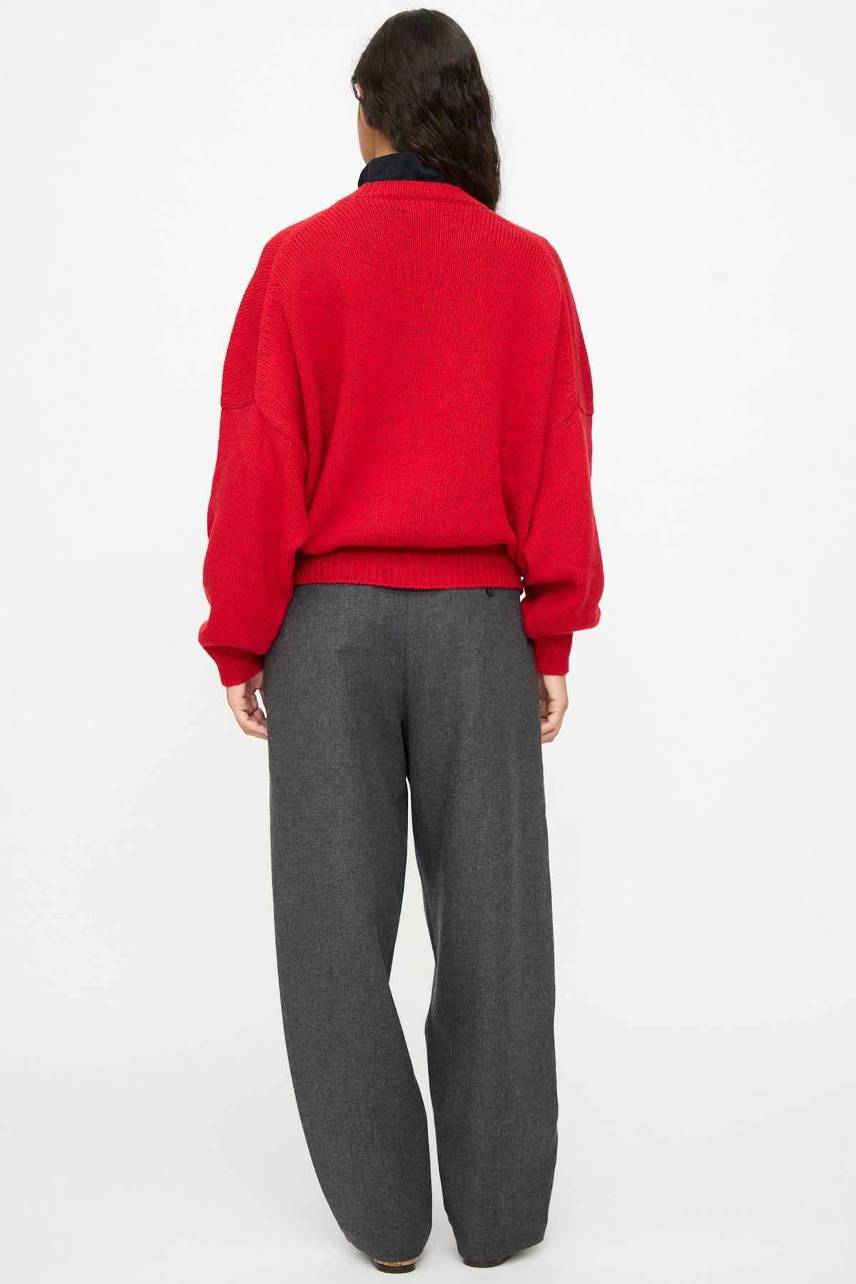 A person viewed from behind wearing an oversized, red Cordera Merino and Cashmere Sweater and grey trousers.