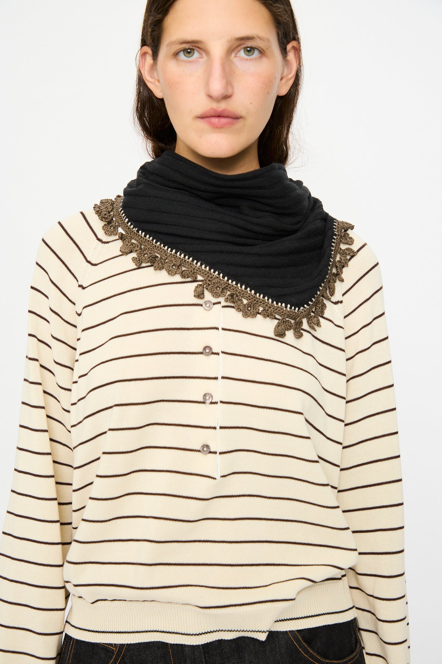 A woman wearing a cream and black striped long-sleeve shirt with decorative buttons and the Cordera Merino Wool Bandana in Black stands against a plain white background.