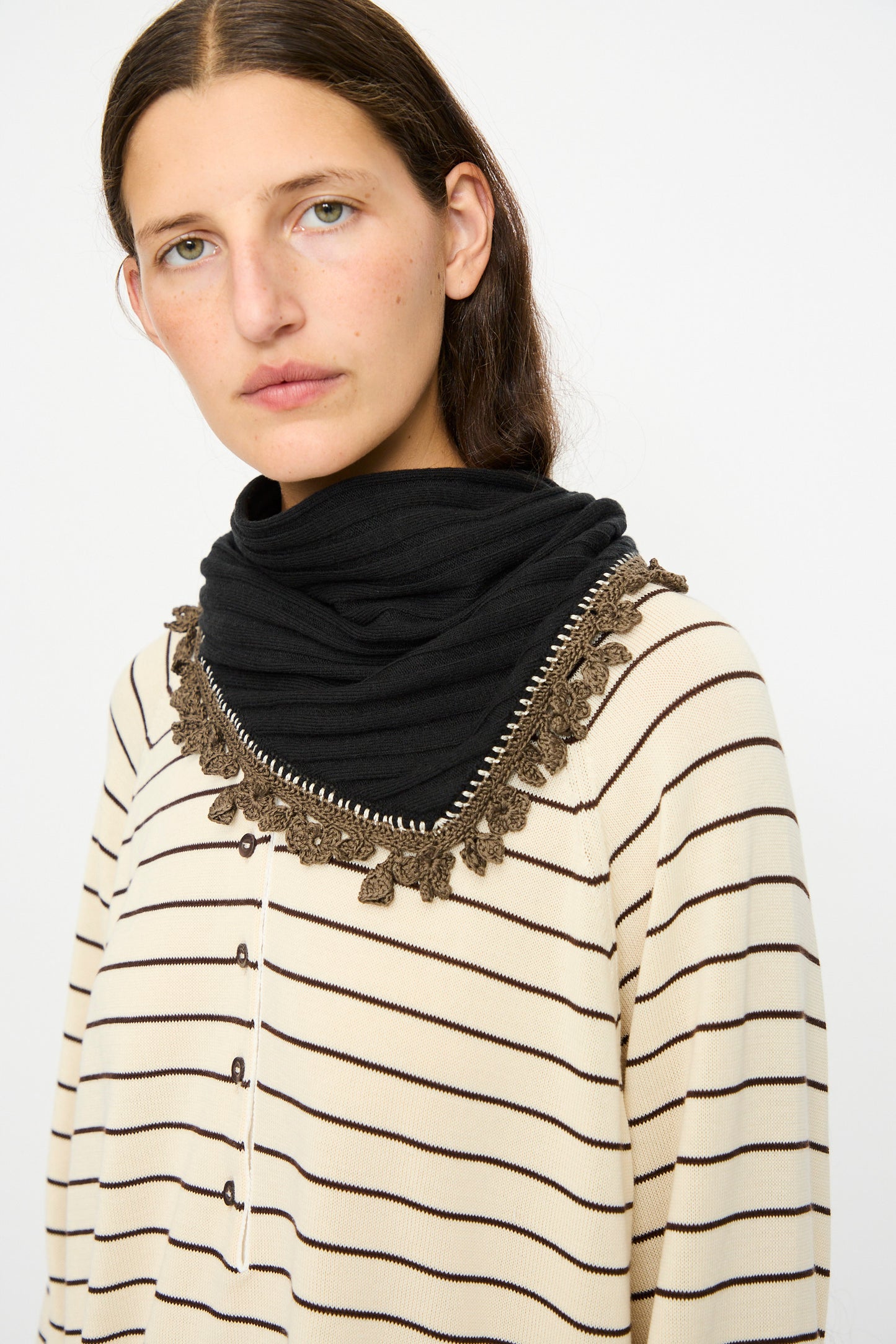 A woman wears the Cordera Merino Wool Bandana in Black and a cream and black striped top with crochet lace trim, standing against a plain white background.