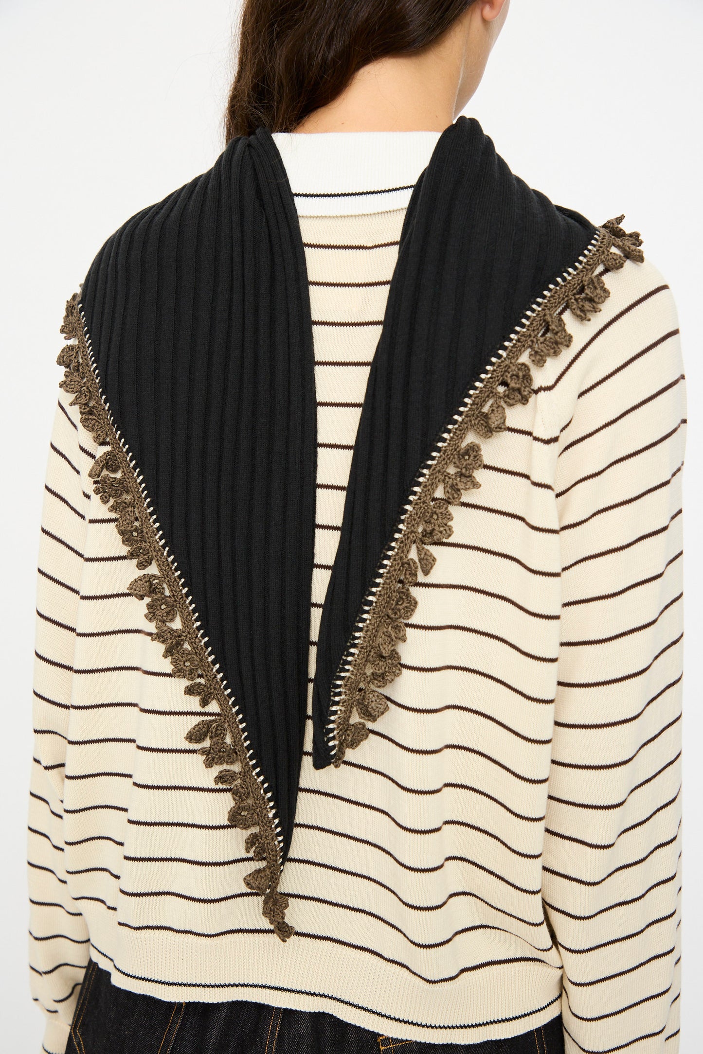 A person wears a cream and black striped sweater with the Cordera Merino Wool Bandana in Black, featuring a triangle shape and brown crochet lace trim, draped elegantly over their shoulders.