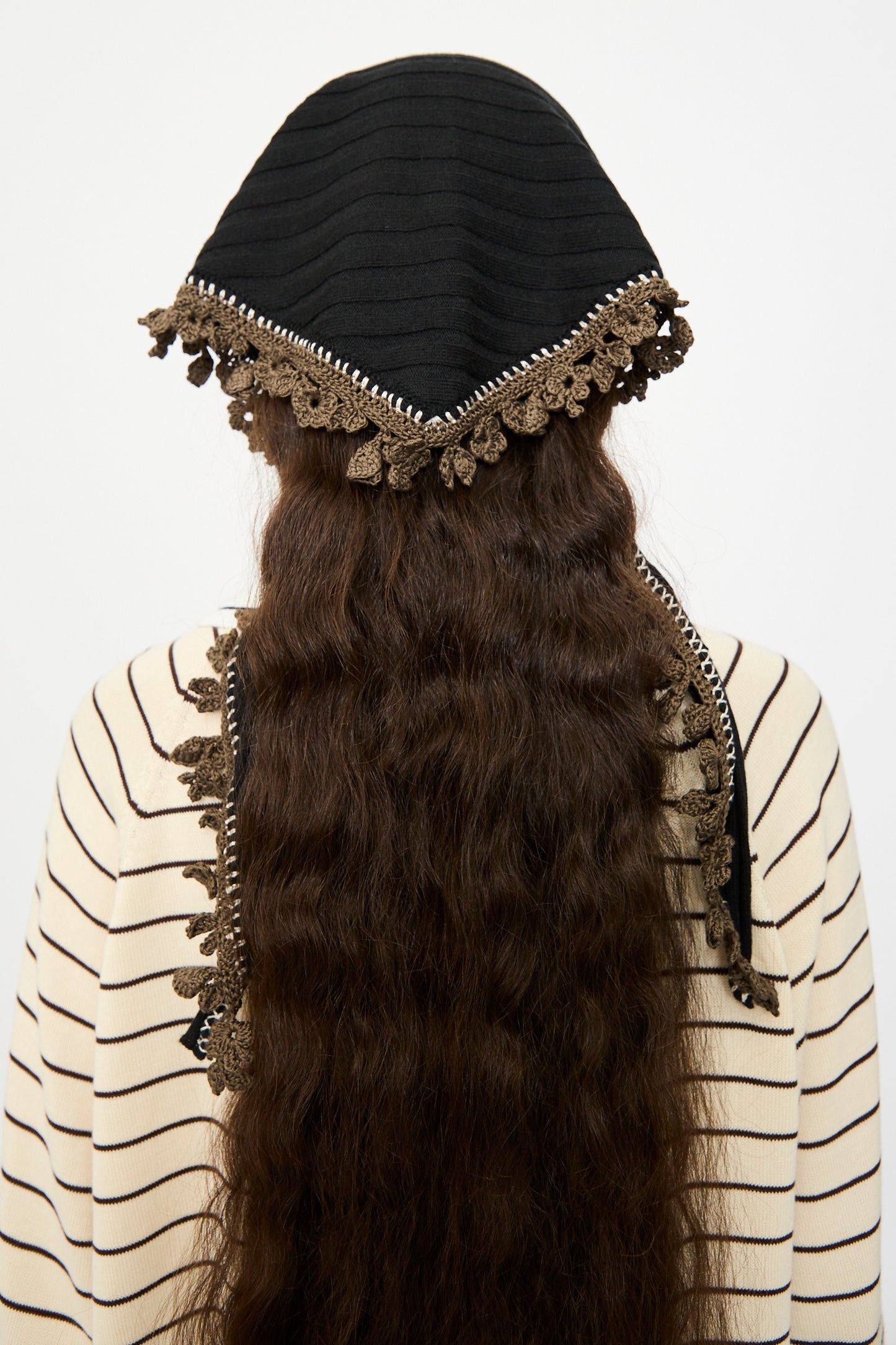 A person with long, wavy brown hair is seen from behind, wearing the Cordera Merino Wool Bandana in Black over a cream and black striped top.