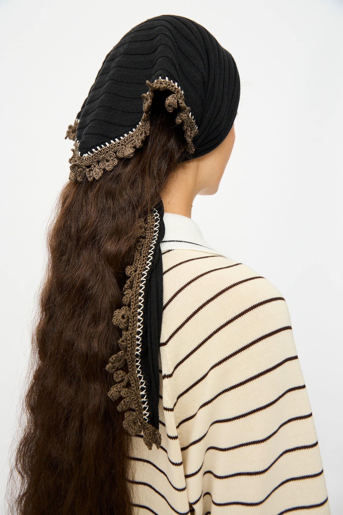 A person with long wavy brown hair wears the Cordera Merino Wool Bandana in Black and a cream and black striped top, shown from the back.
