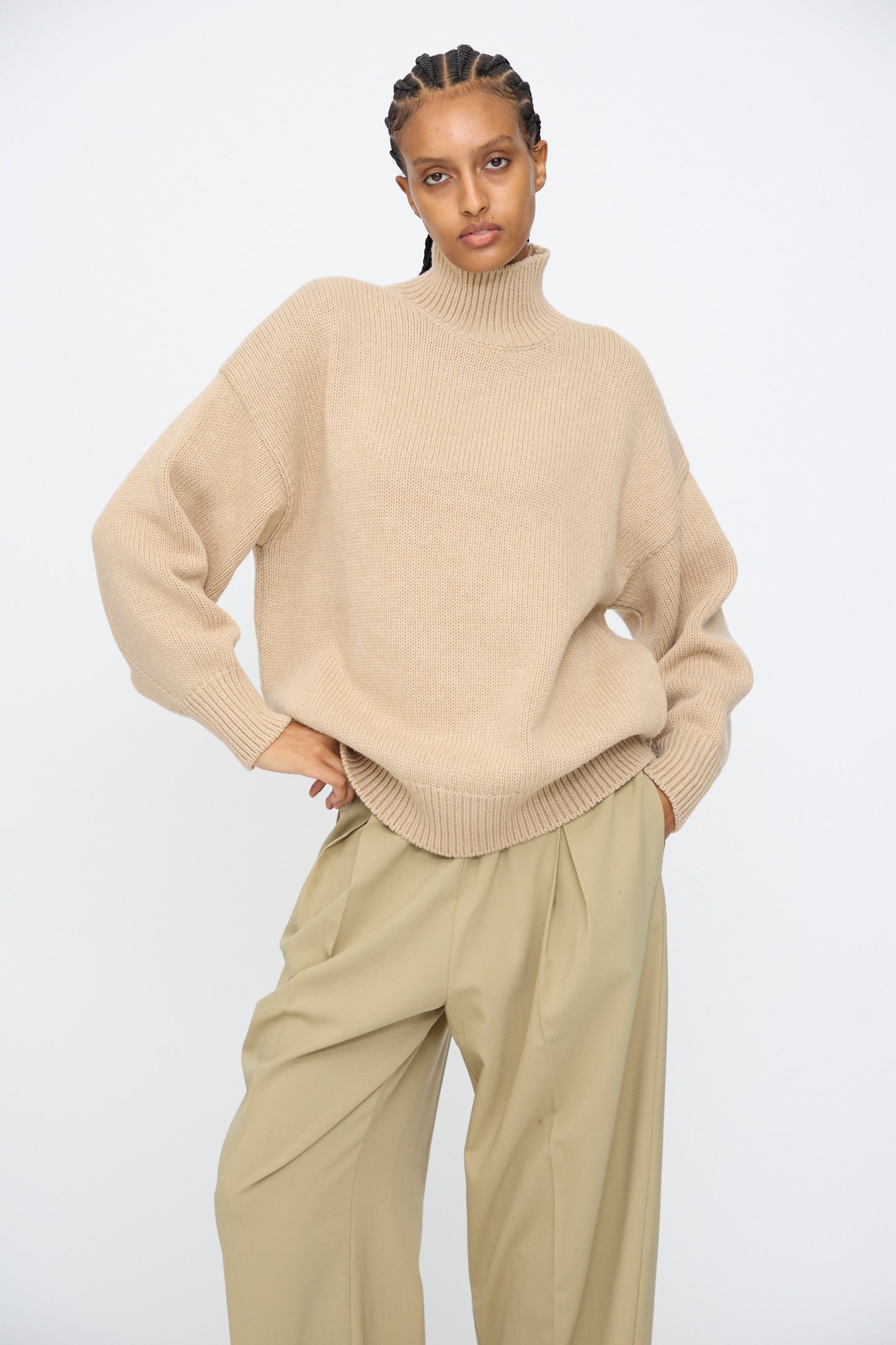 Model wears the Cordera Merino Wool Chunky Turtleneck Sweater in Beige with loose-fitting khaki pants, standing against a plain white background.