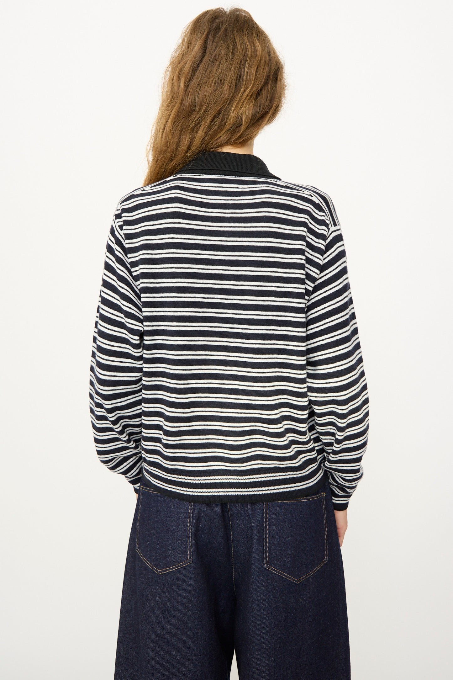 Model with long, wavy hair wears the Cordera Merino Wool Polo Cardigan in Striped and dark wide-leg jeans, shown from the back against a plain white background.