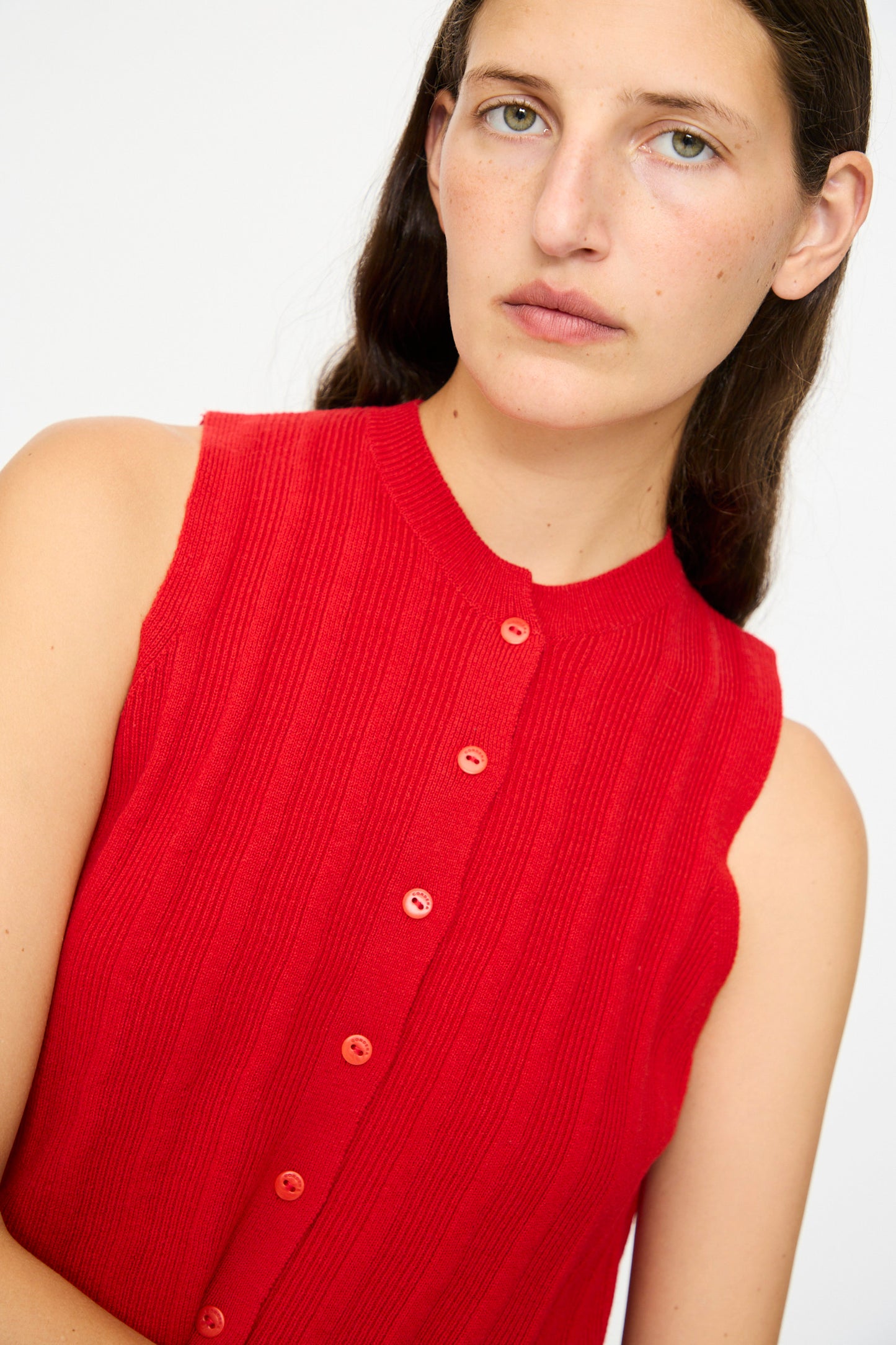 A person with long brown hair wears the Cordera Merino Wool Ribbed Waistcoat in Red, styled sleeveless and cropped, looking toward the camera against a plain light background.