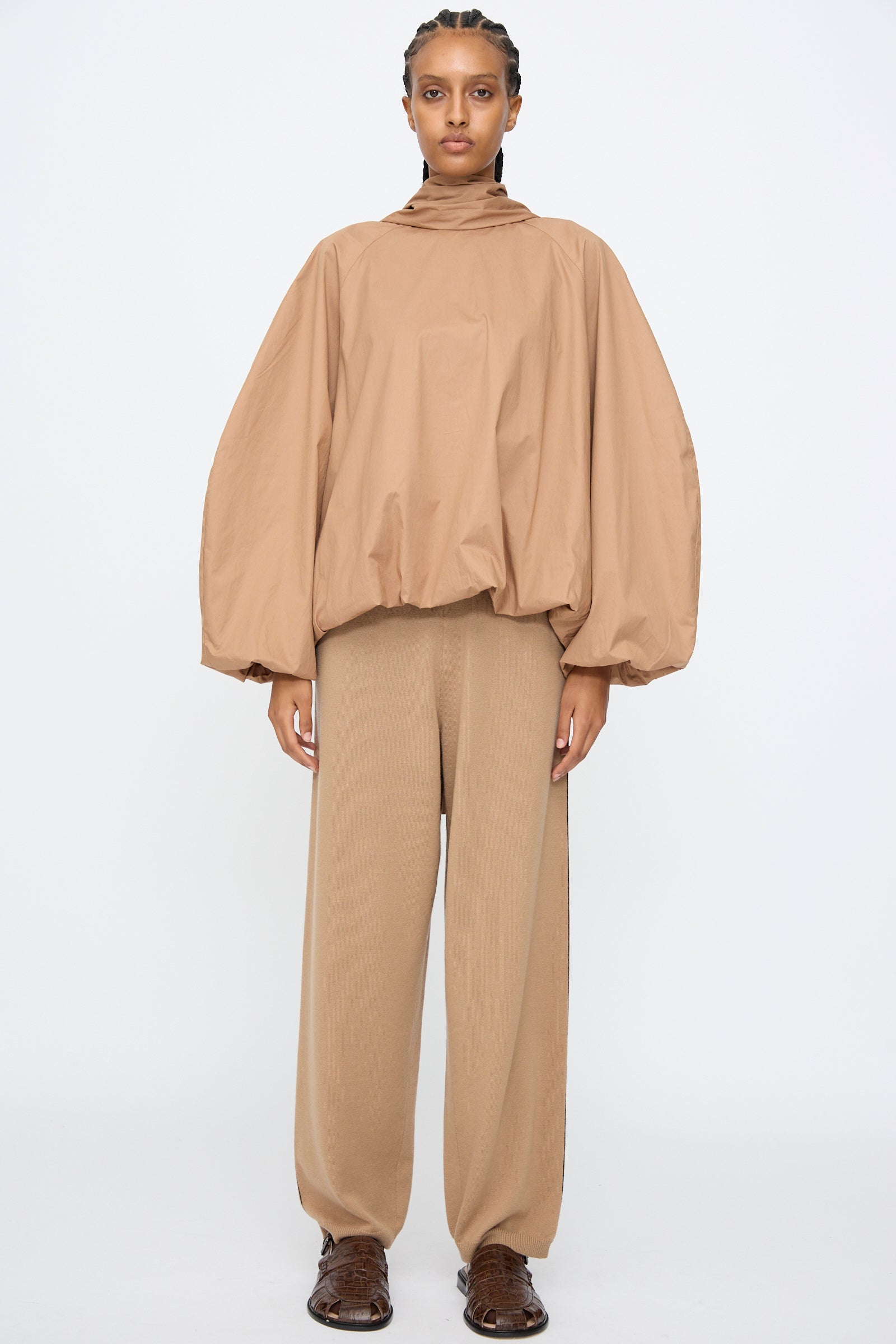 A person stands against a plain background wearing Cordera’s Merino Wool Straight Pants in Camel, paired with a matching oversized tan balloon-sleeve top and brown shoes.