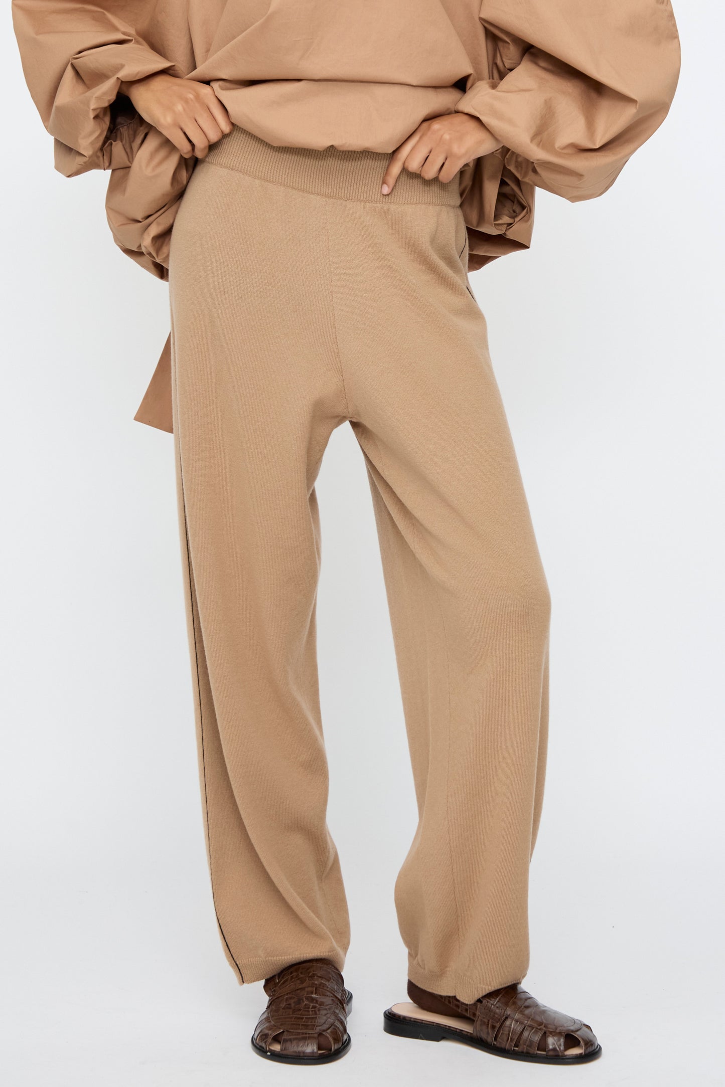 A person wears Cordera Merino Wool Straight Pants in Camel with an oversized beige top and brown crocodile-textured sandals, standing against a plain white background.