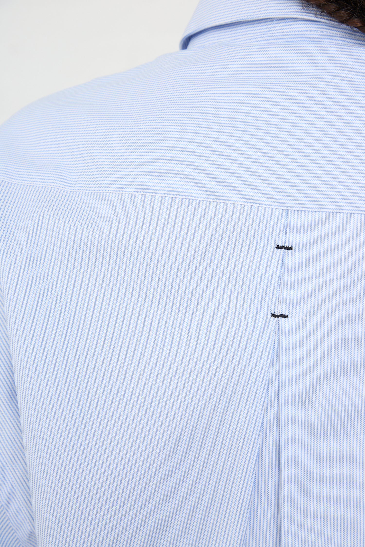 A close-up of the back of a person wearing an oversized, striped shirt made in Spain, with a detail showing the yoke and pleat with buttons - Cordera's Organic Oxford Shirt in Blue.