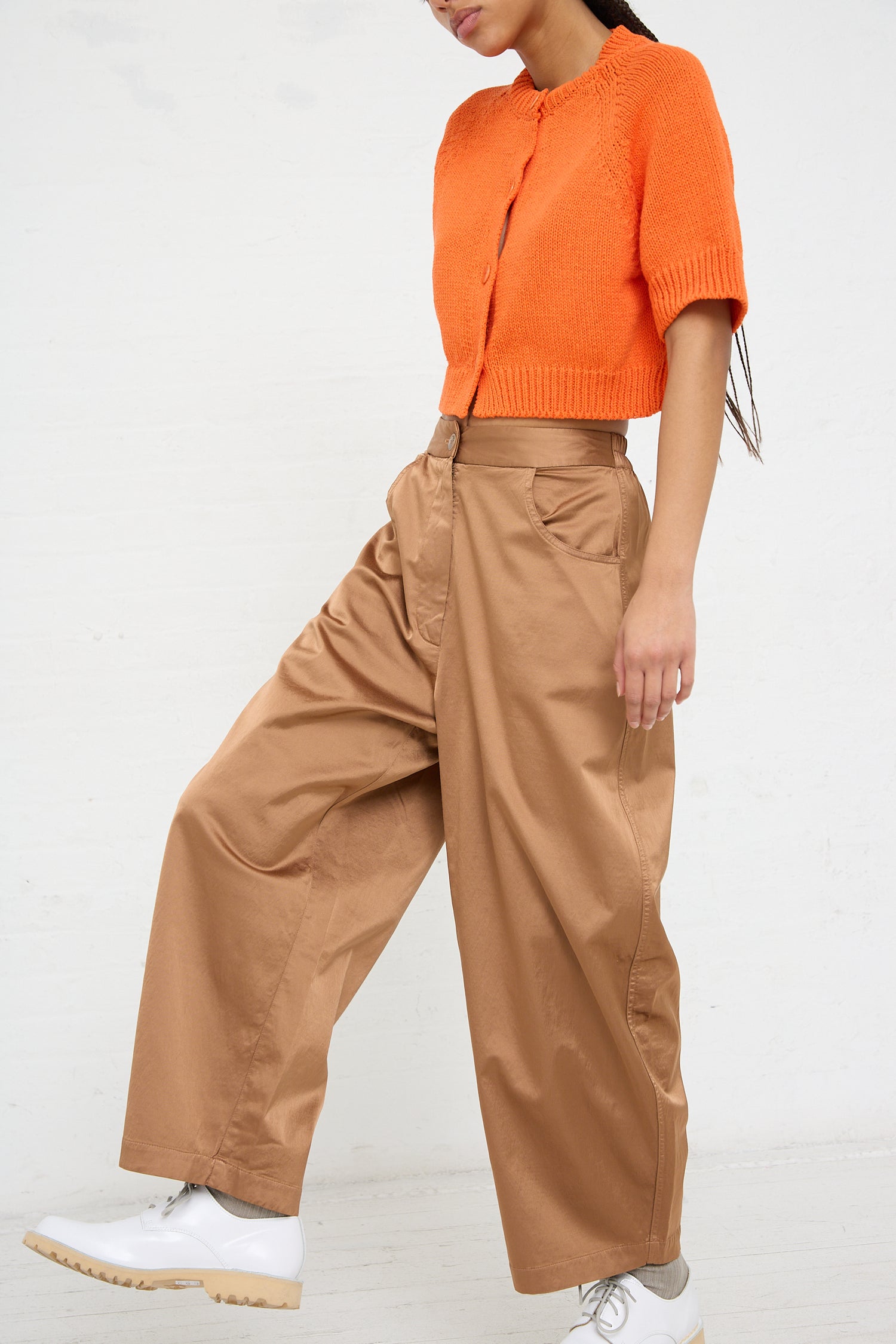 Woman in bright orange top and Cordera high-rise, wide-leg brown Satin Curved Pant in Camel standing against a white background.