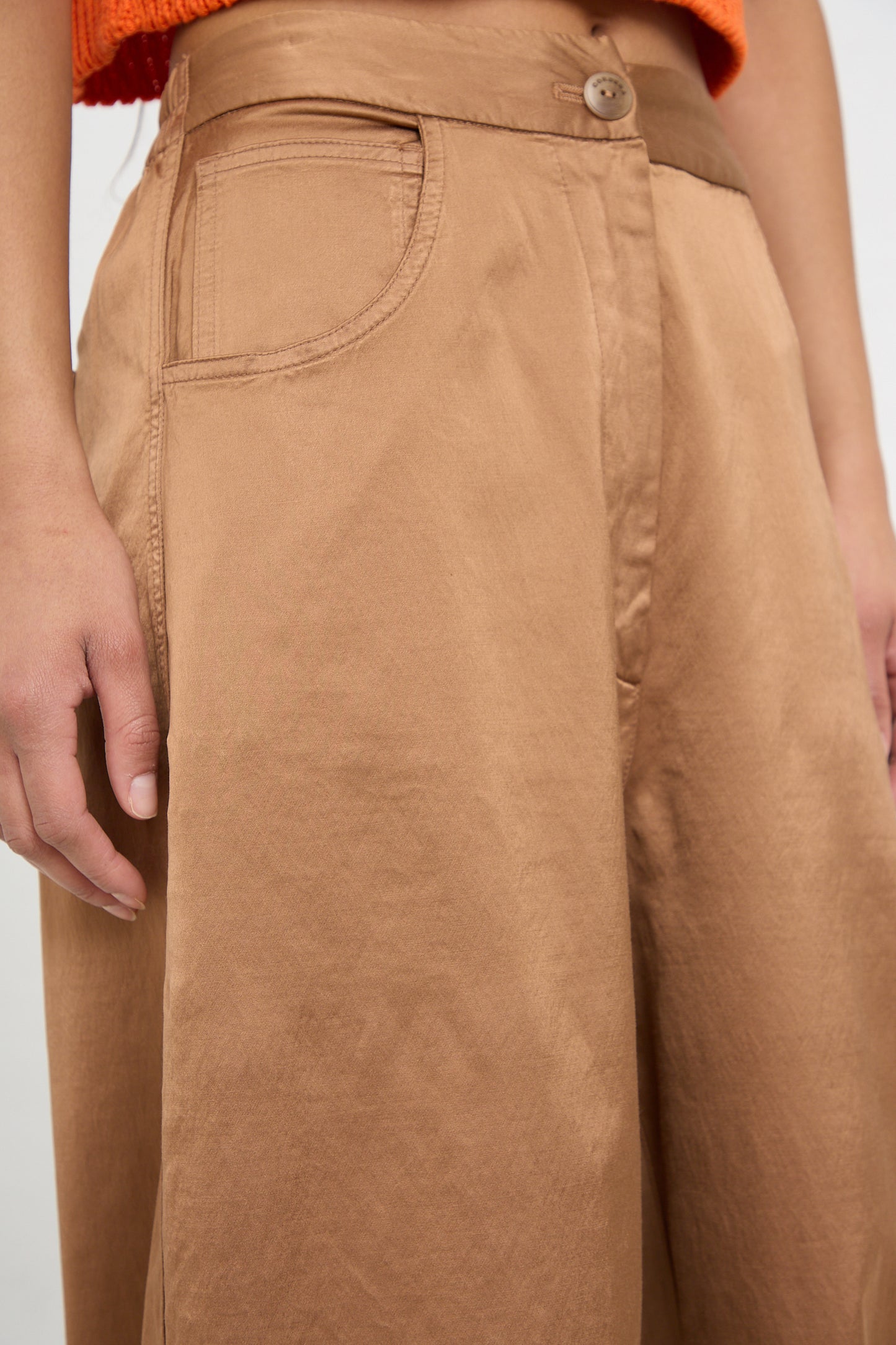 Close-up of a person wearing Cordera's Satin Curved Pant in Camel with a detailed view of the high-rise waistband and pocket, emphasizing ethical fashion.