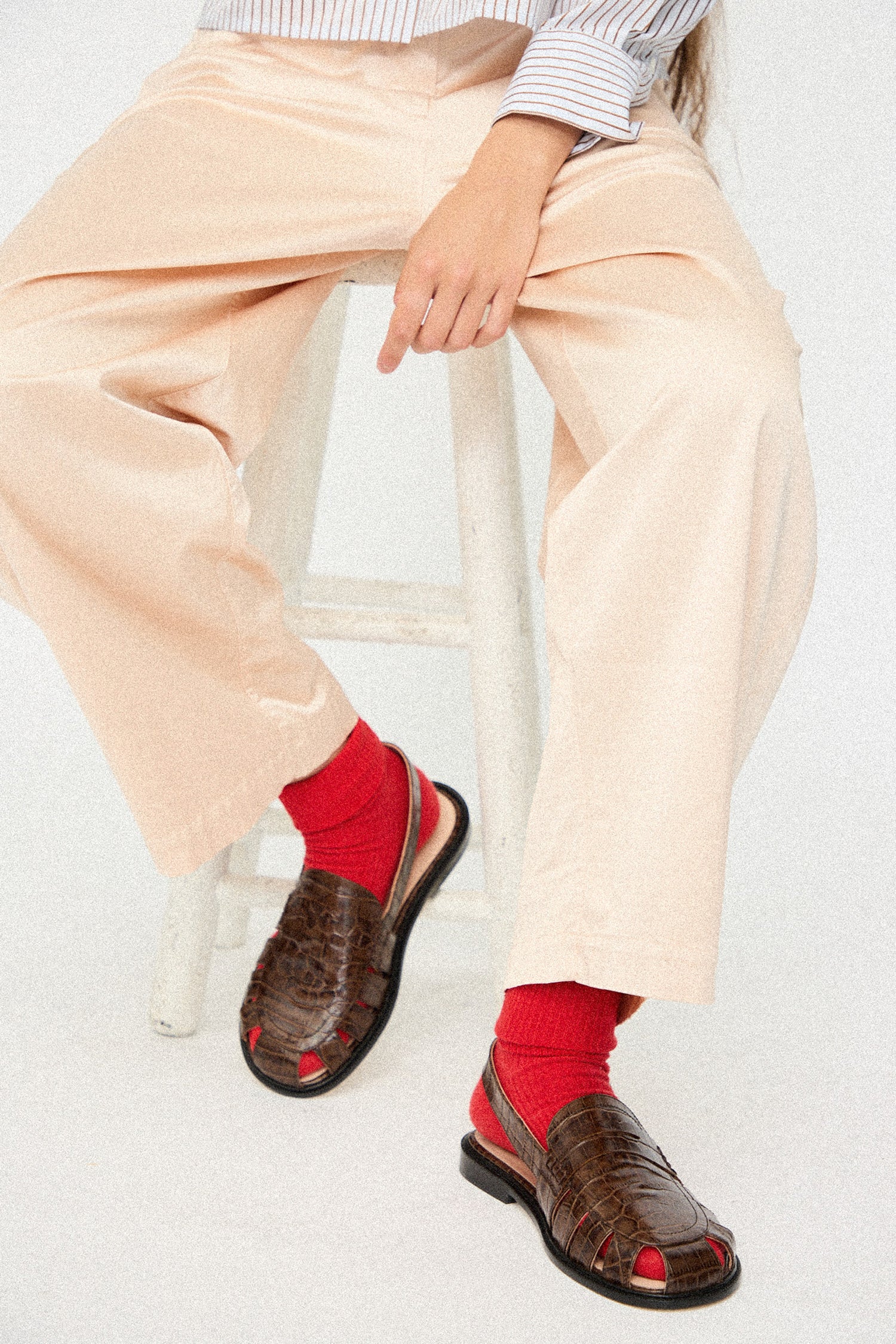 Person wearing beige pants, red socks, and brown sandals on a white background