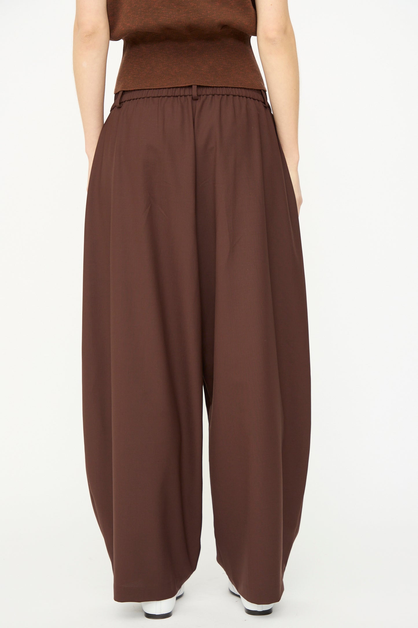 A person wears Cordera's Tailored Crossover Pant in Burgundy, featuring a loose fit, wide legs, and high waist, with hands in pockets, shown from the front against a plain white background.