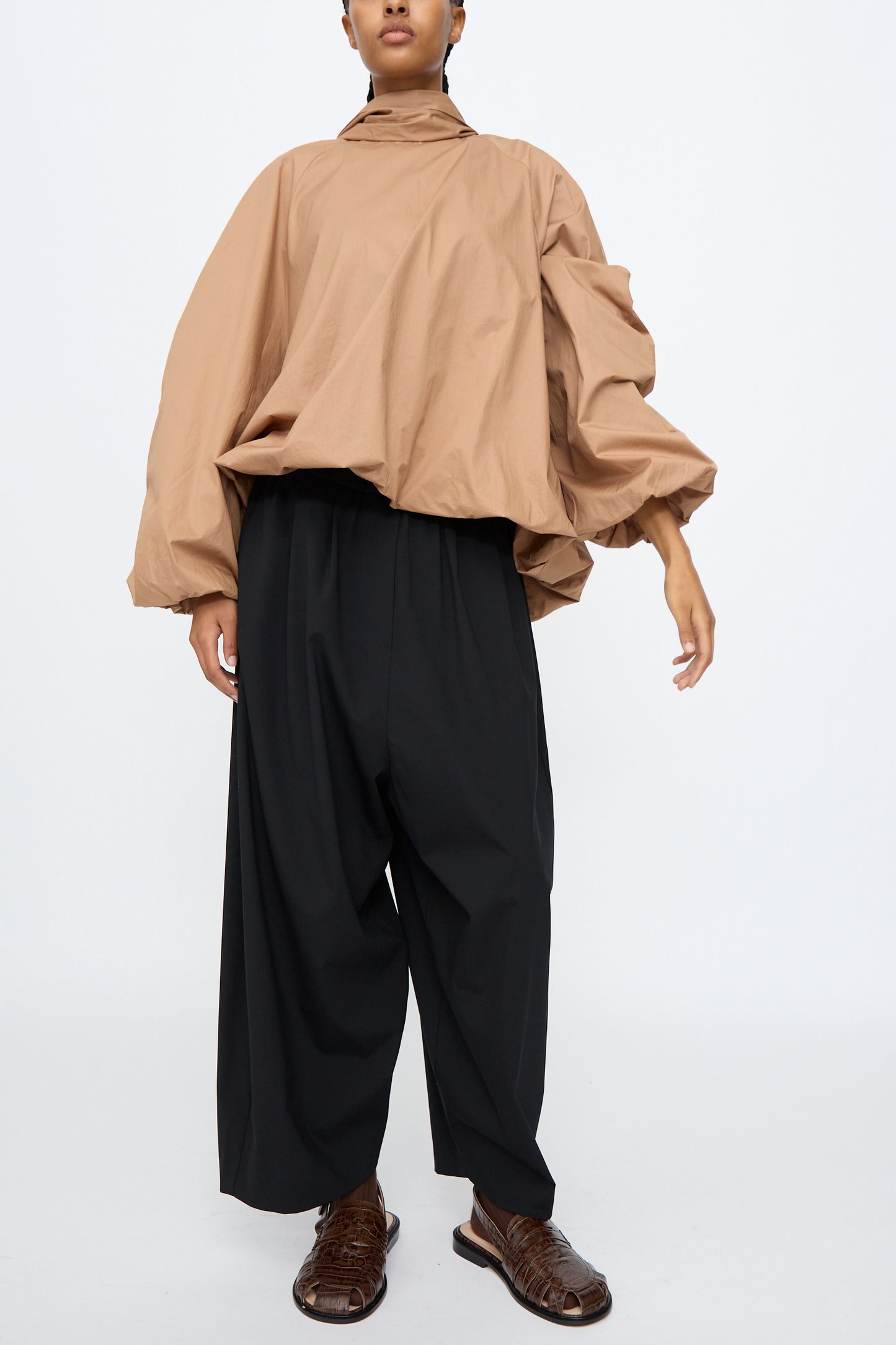 A person wearing a loose tan long-sleeve top, Cordera's Tailoring Maxi Pants in Black with an elastic waistband, and brown woven shoes stands against a plain white background.