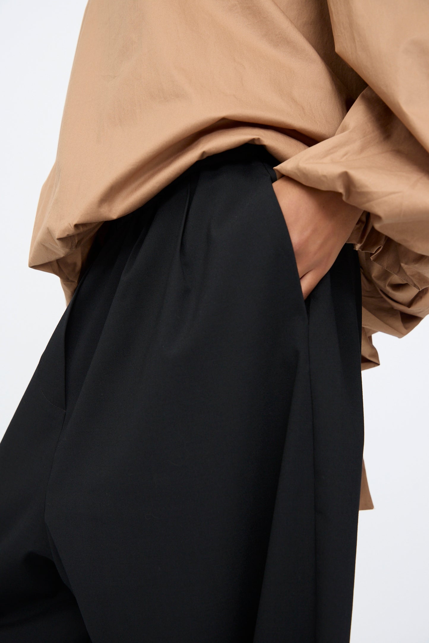 A person wears the Cordera Tailoring Maxi Pants in Black—high-waisted, oversized, with an elastic waistband—and a loose beige blouse with billowy sleeves, one hand tucked into the pocket.