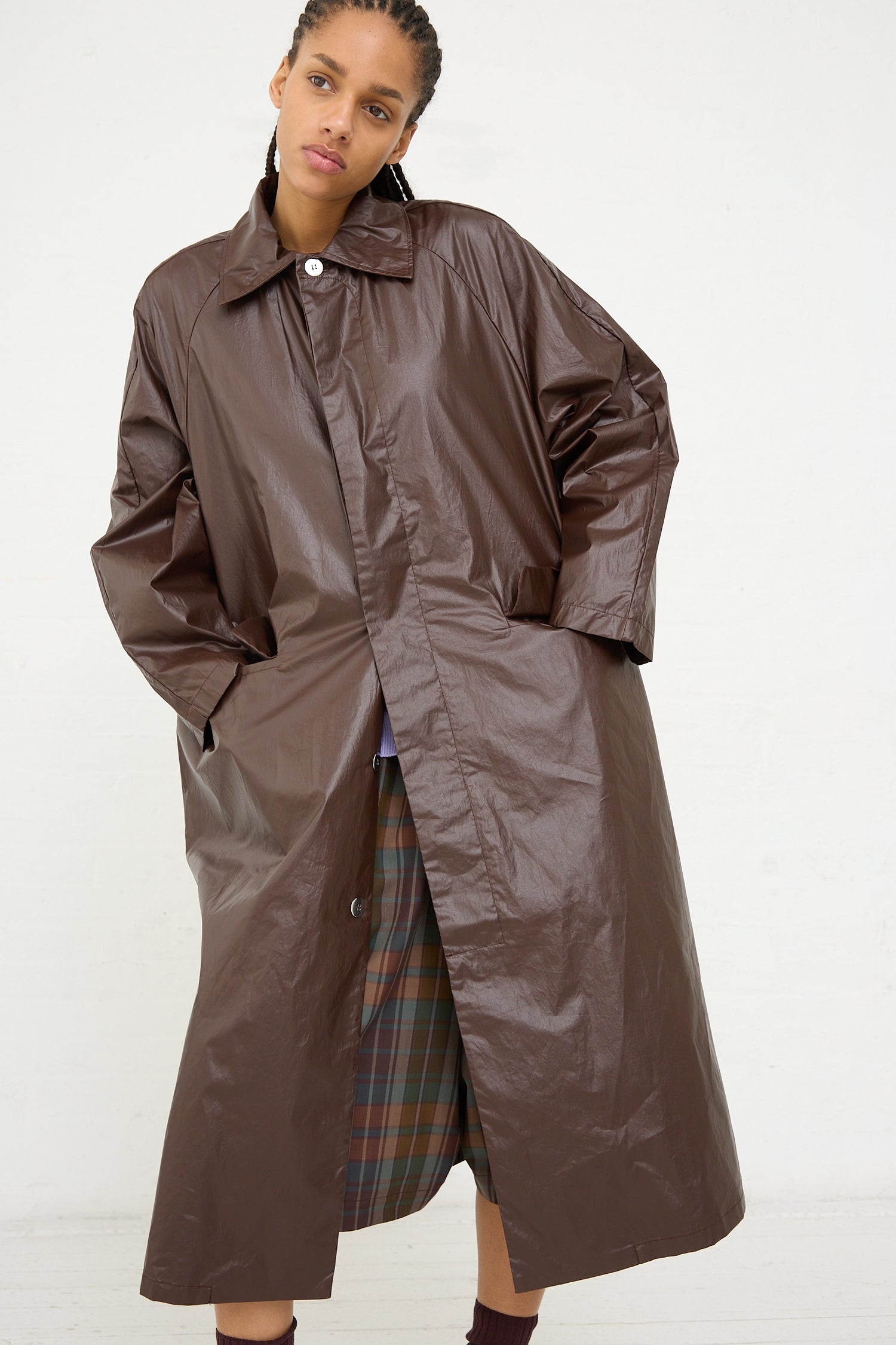 A woman modeling a water-repellent, long brown Cordera trench coat in Prune with a plaid skirt visible underneath.