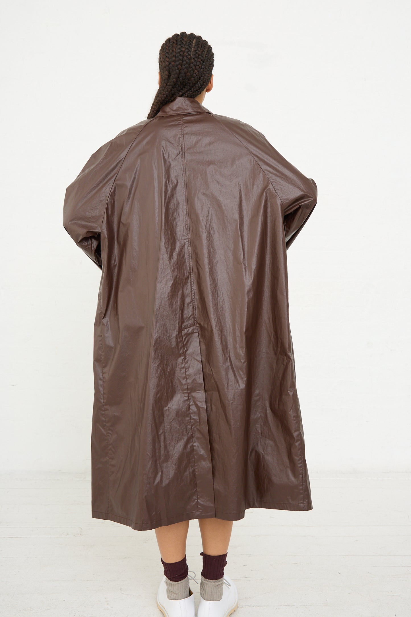 Person standing with their back to the camera wearing a long Prune water-repellent trench coat from Cordera and white sneakers.