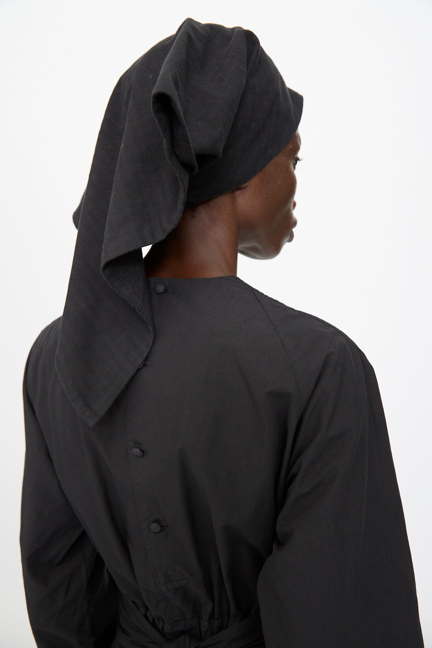 A person shown from behind against a plain background wears a long-sleeved black garment with button details and the Cosmic Wonder Double Gauze Check Hair Scarf in Black.