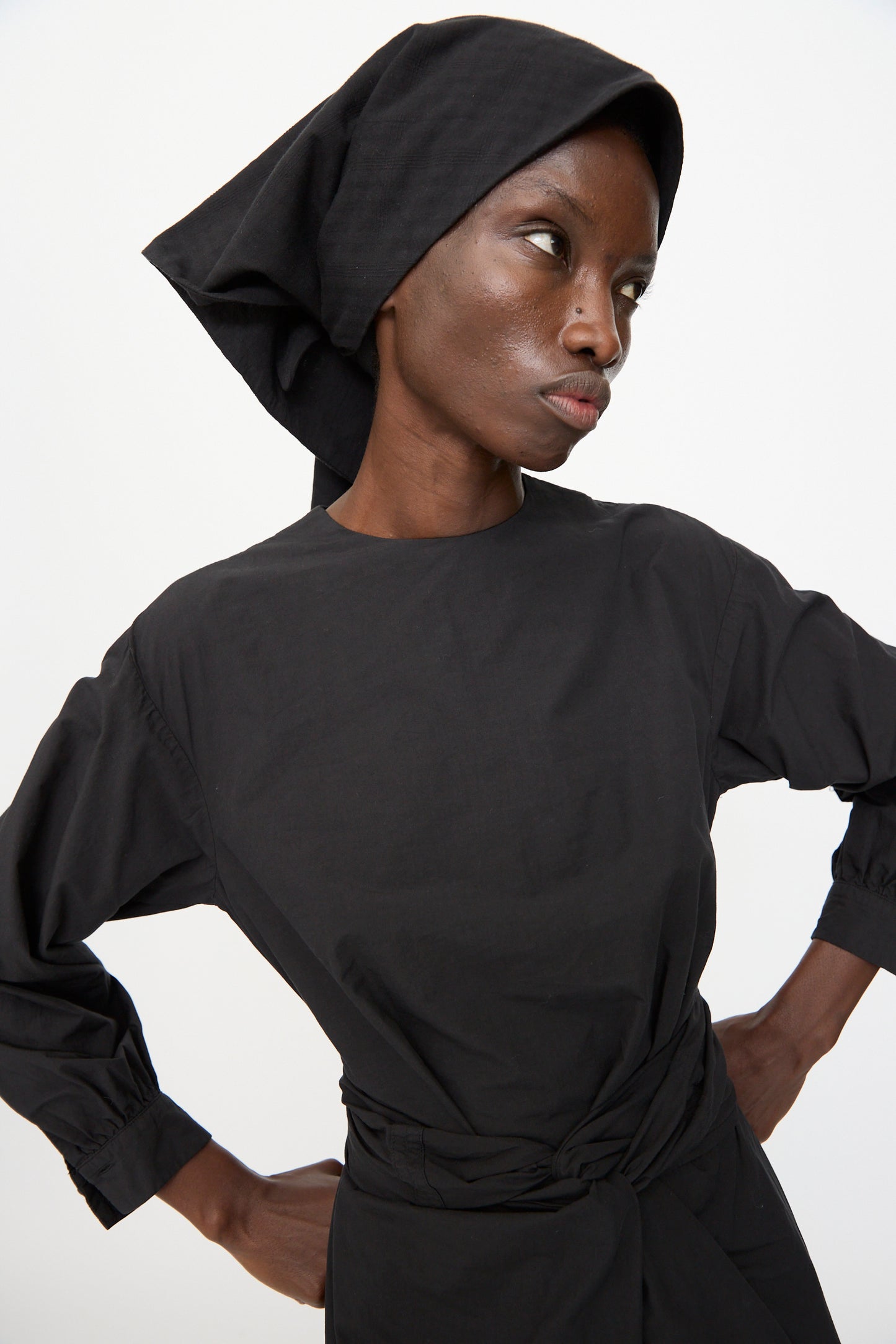 Model wears the Cosmic Wonder Double Gauze Check Hair Scarf in Black, styled with a black long-sleeve top, standing hands on hips and looking to the side against a plain background.