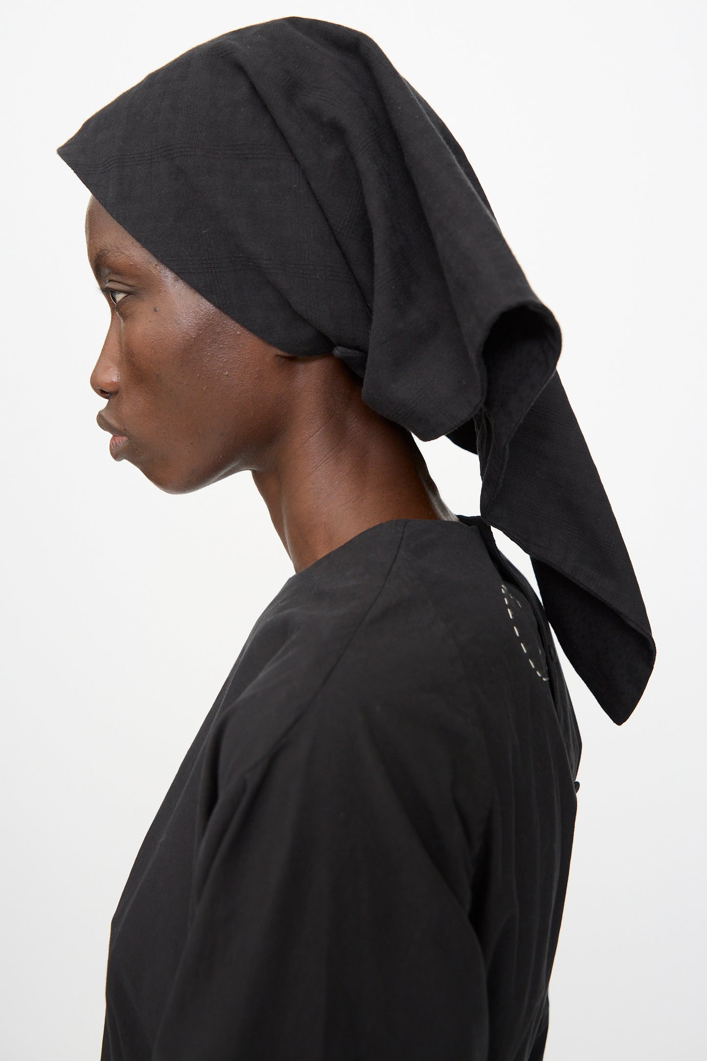 A person in profile view wears the Cosmic Wonder Double Gauze Check Hair Scarf in Black with black clothing, standing against a plain white background.