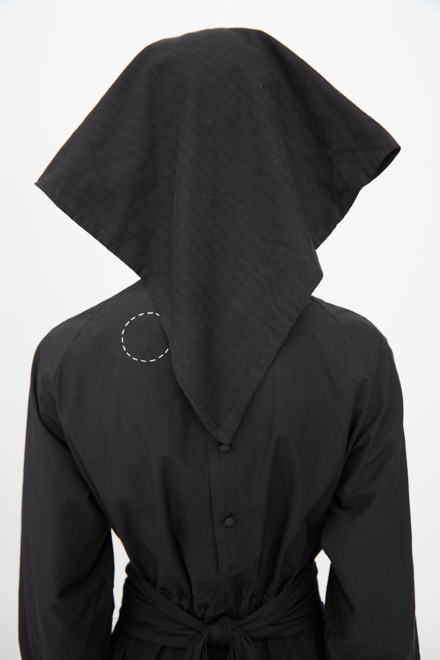 A person stands facing away, wearing the Cosmic Wonder Double Gauze Check Hair Scarf in Black, draped over their head and featuring a stitched circle detail on the upper back.
