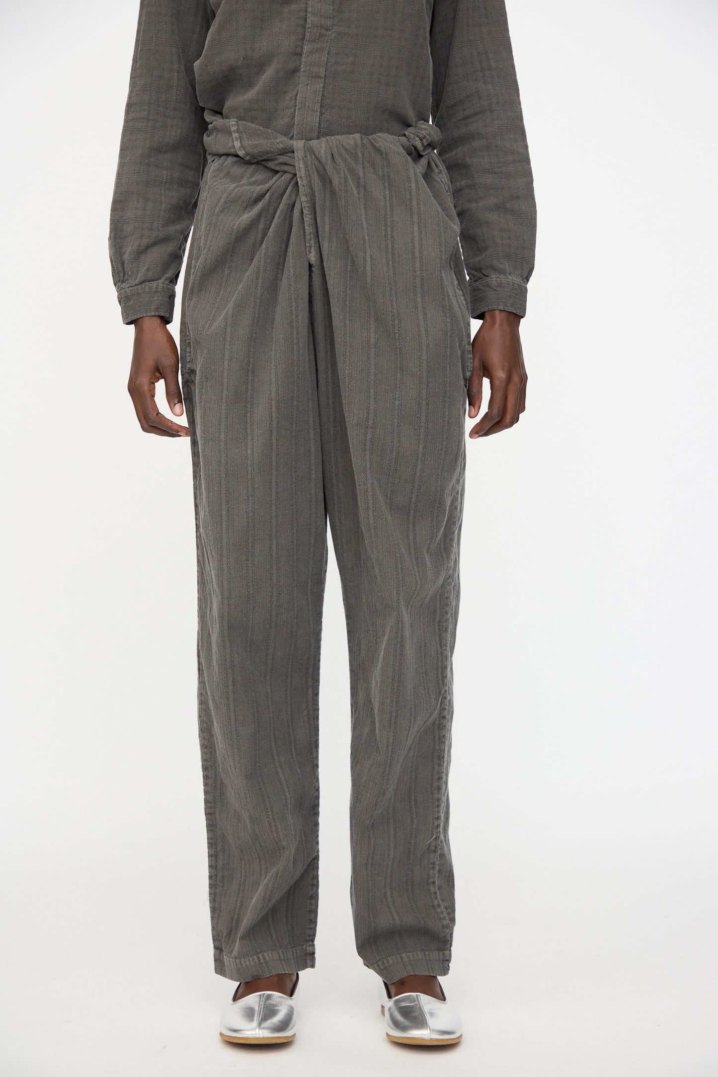 A person models Cosmic Wonder's Stripe Combination Wrapped Pant in Dark Sumi with a matching top and silver slip-on shoes, standing against a plain white background.