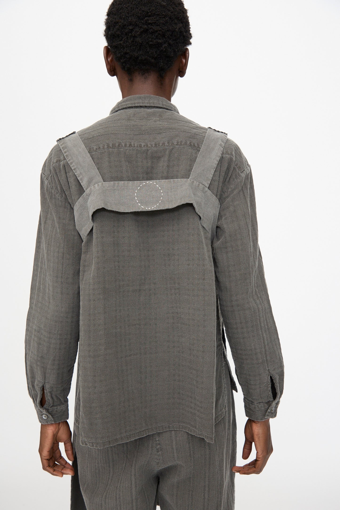 Person wearing Cosmic Wonder's Taskuki Apron in Dark Sumi, a loose-fitting, textured gray apron-inspired garment, standing against a plain white background.
