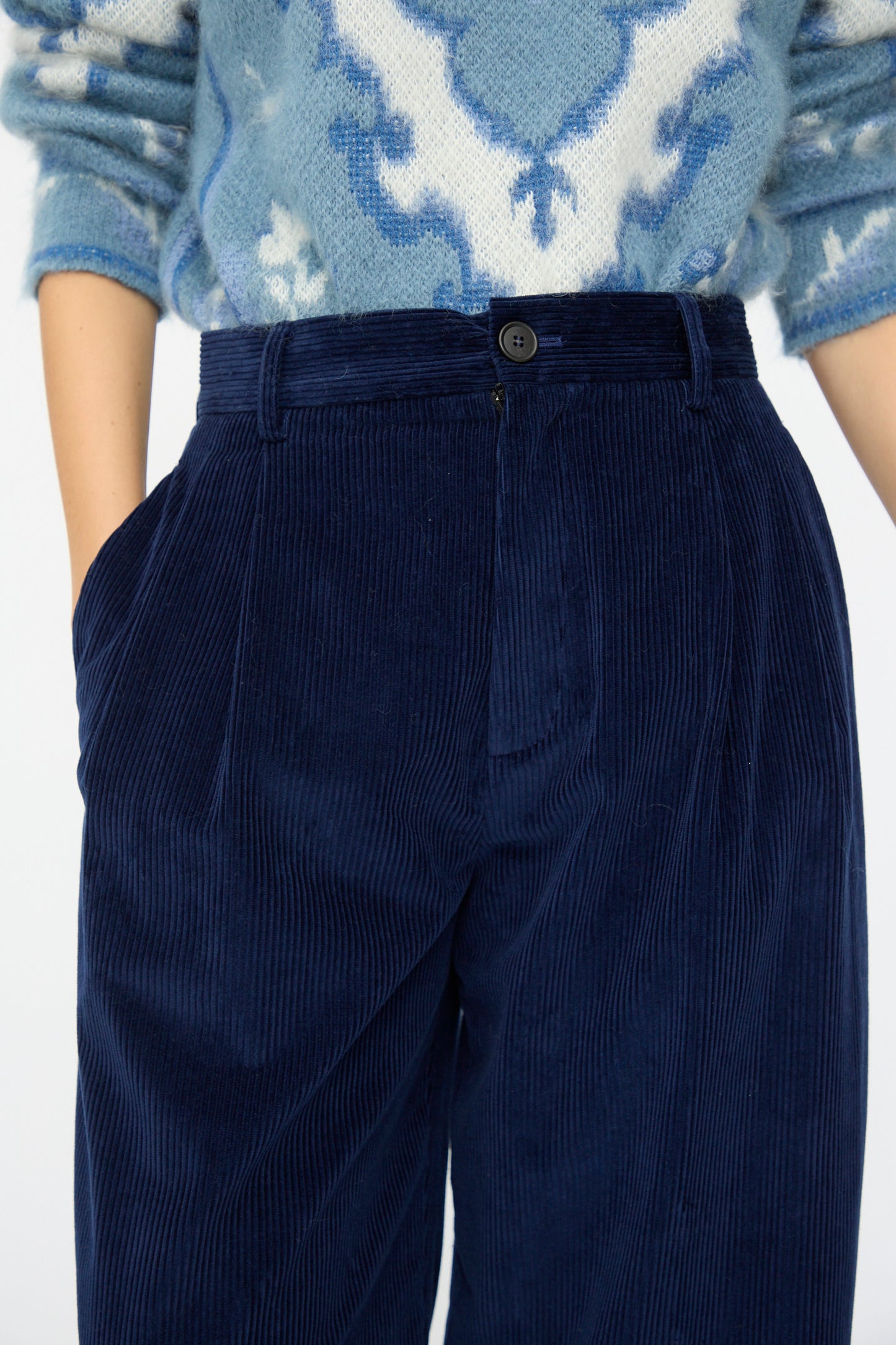 Model wears Cristaseya Corduroy Double Pleated Wide Pants in Indigo, styled with hands in pockets and paired with a blue patterned sweater.