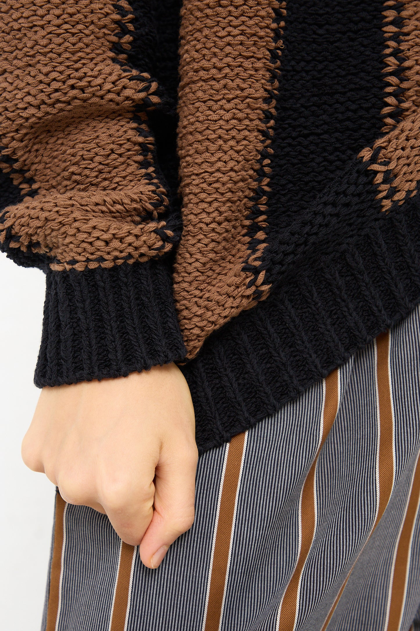 A woman wearing a Cristaseya Fettuccia Striped Sweater in Black and Noisette and striped pants. Up close view.