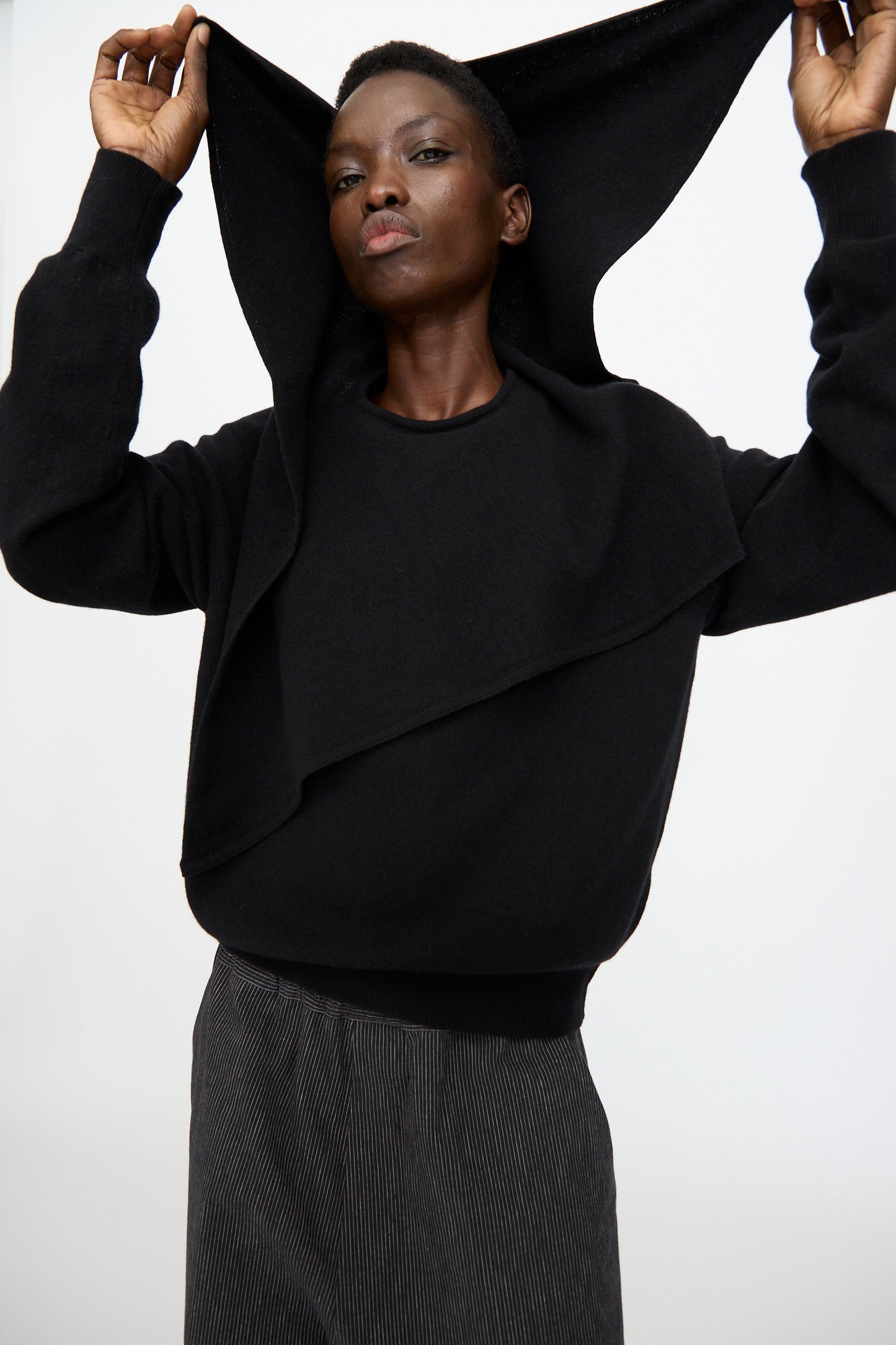 A person wears the Cristaseya Flannel Sailor Collar Sweater in Black, lifting part of the garment over their head while standing against a plain white background.