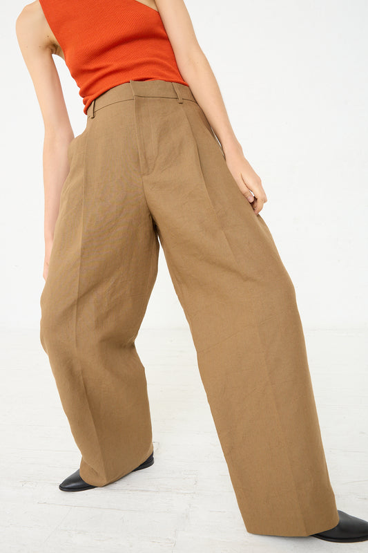 A woman in an orange top and tan pants, wearing Cristaseya's Japanese Washi and Linen Canvas Double Pleated Wide Trouser in Mocha, is confidently posing.
