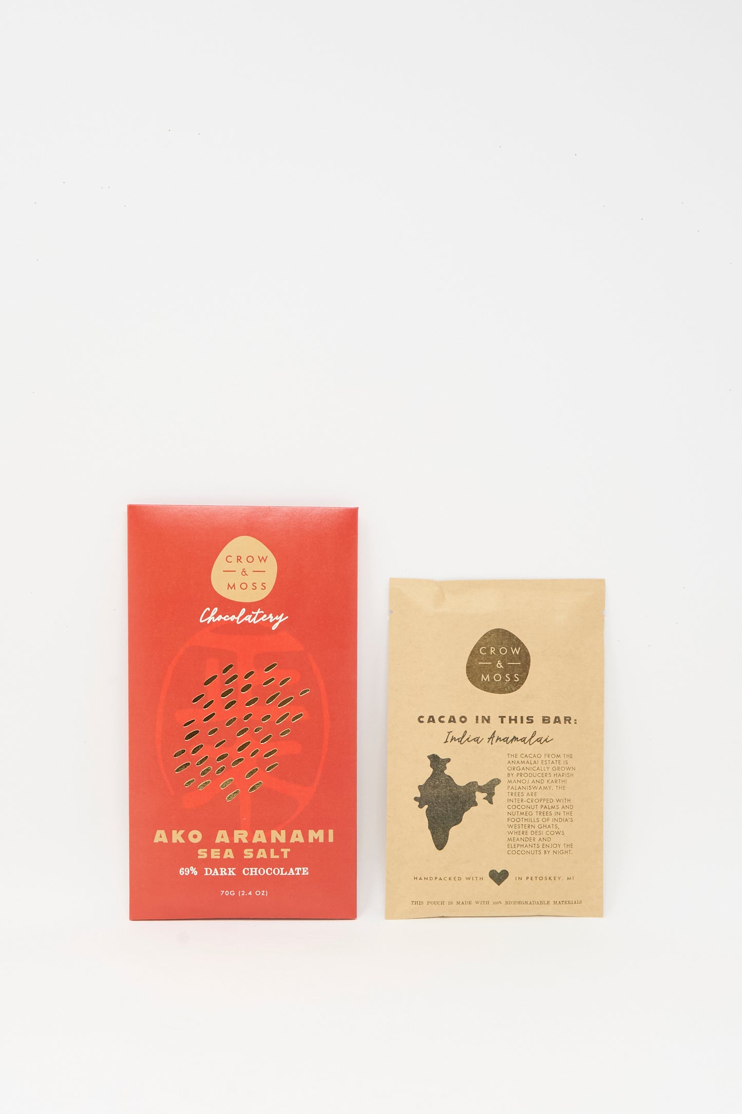 A red wrapper labeled “Ako Aranami Sea Salt Dark Chocolate” by Crow & Moss, featuring Japanese sea salt, lies next to a brown card displaying a map of India and details on single origin cacao sourcing.