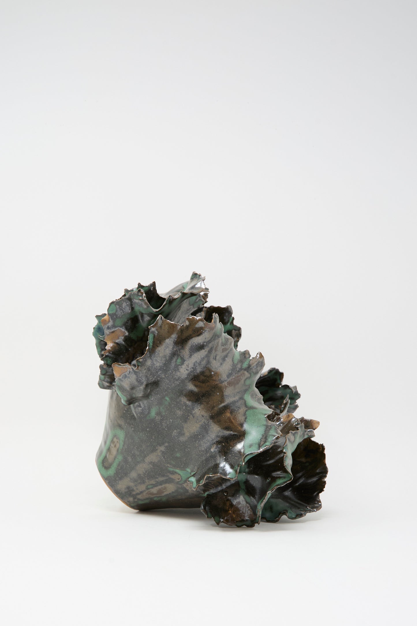 Wild Petals Iris N.5 in Green by Dear You: an abstract ceramic sculpture featuring wavy, textured edges and a dark green, glossy finish, reminiscent of a porcelain vase, set against a plain white background.
