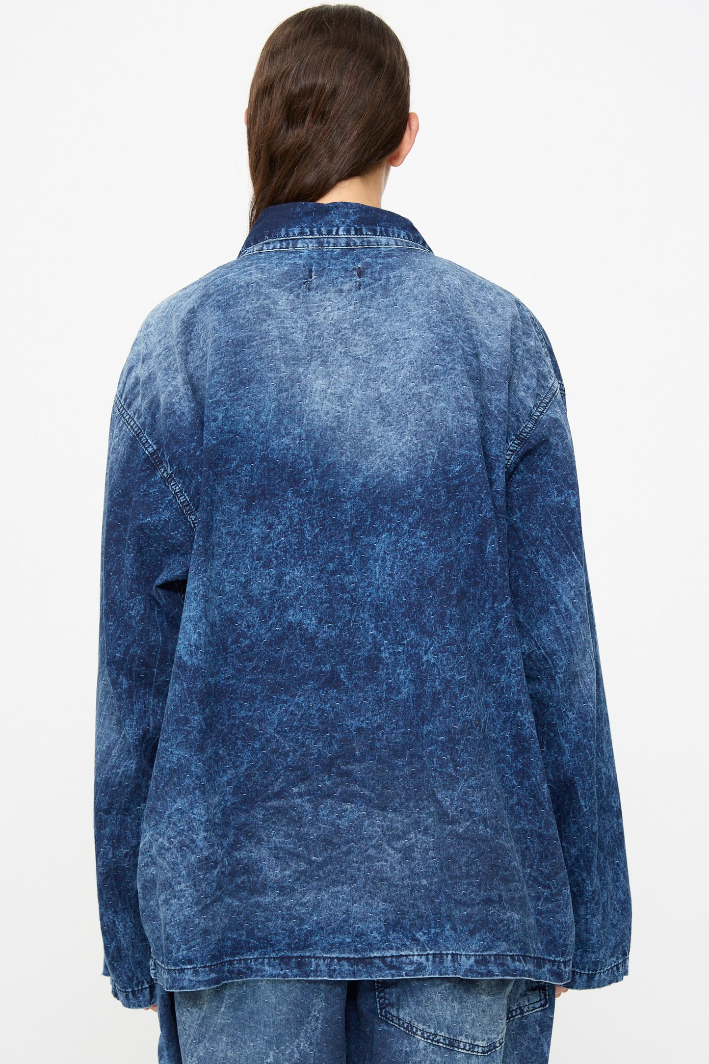 A person with long brown hair is shown from the back against a plain white background, wearing the Dr. Collectors 6 oz. Cotton New Saigon Shirt Jacket in Indigo along with matching denim jeans.