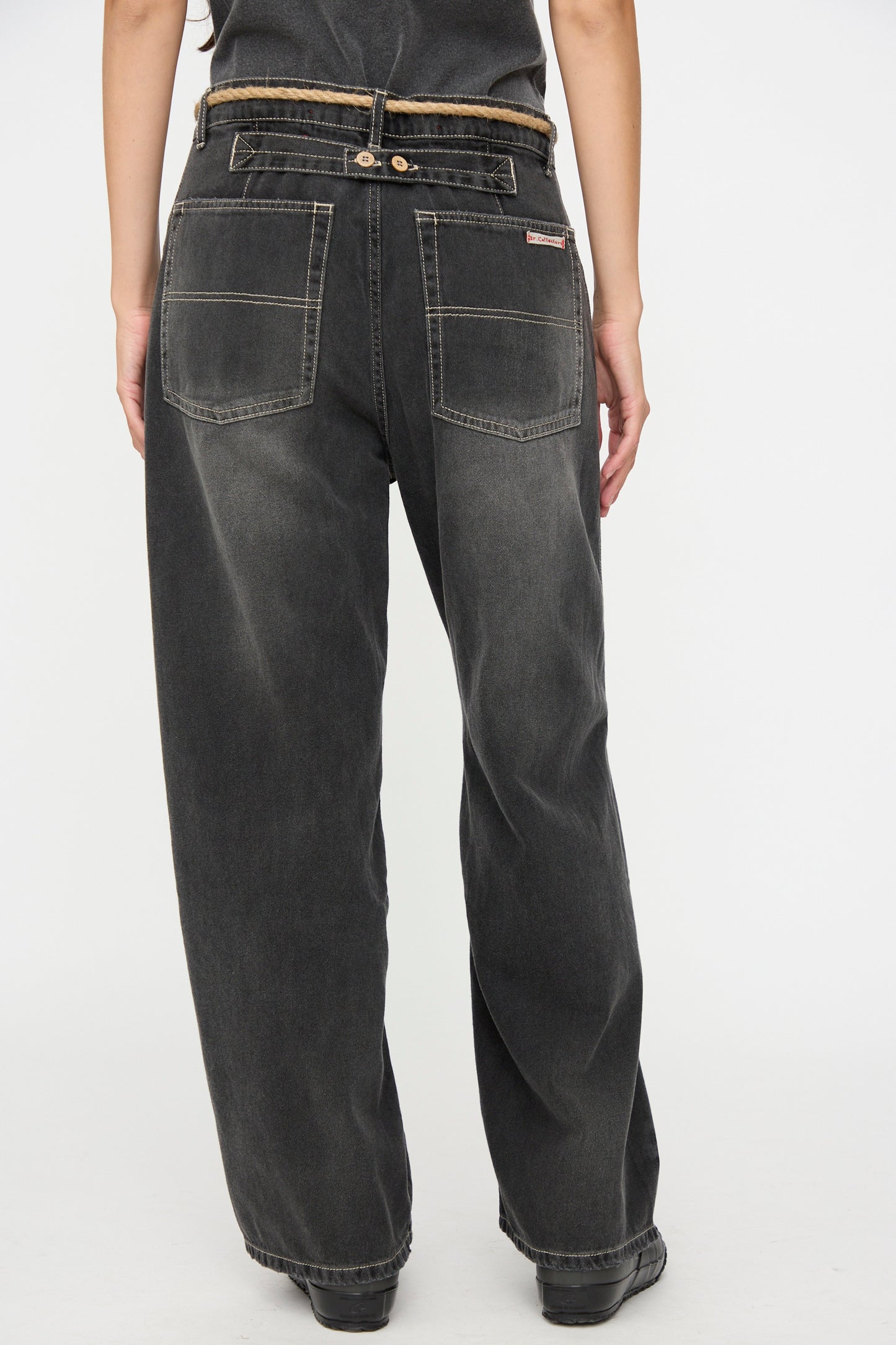 A person is shown from the back against a plain white background, wearing Dr. Collectors’ 9 oz. Denim P84 Dungaree Pant in Sunfaded Black, featuring a loose fit, large back pockets, and a braided hemp rope belt.